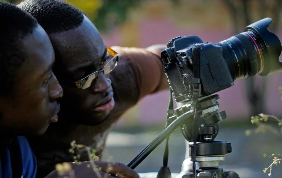 Two men looking through a telescope mounted on a tripod, outdoors during daytime.