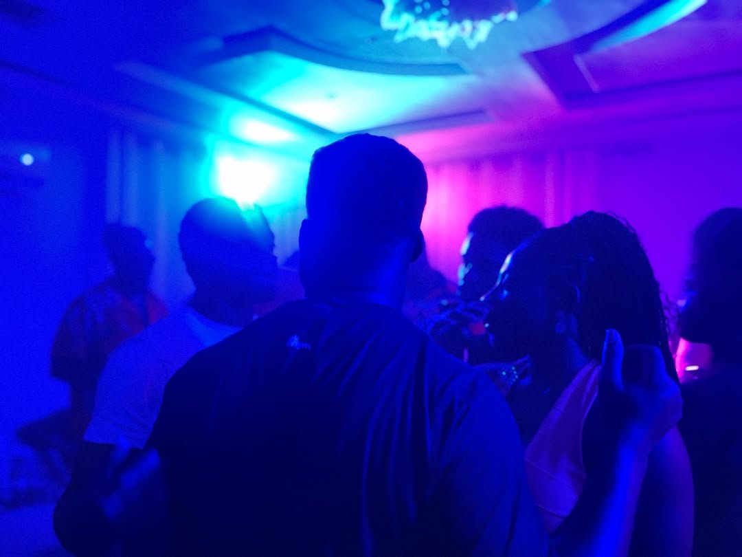 People dancing and socializing in a dimly lit nightclub with blue and pink lighting.