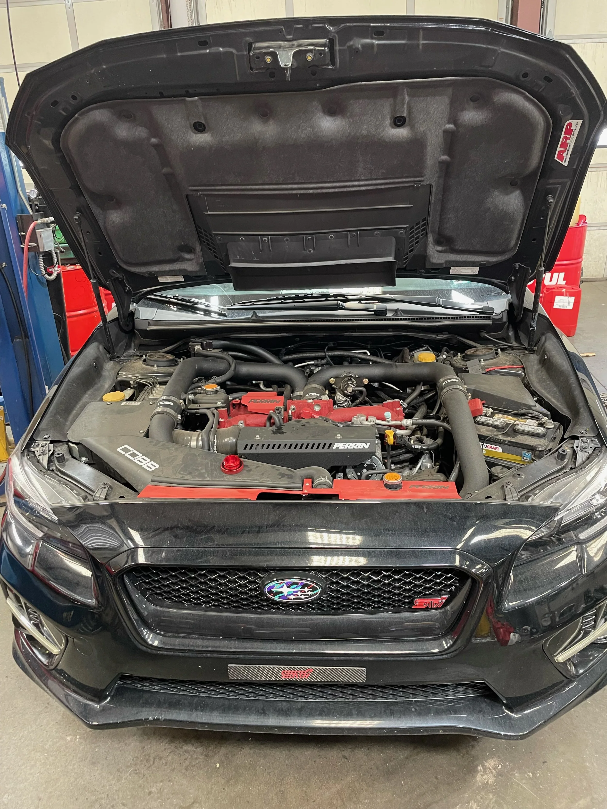 View of a Subaru WRX STi engine compartment with various components including a blue intake pipe, radiator, and other aftermarket engine components STi.
