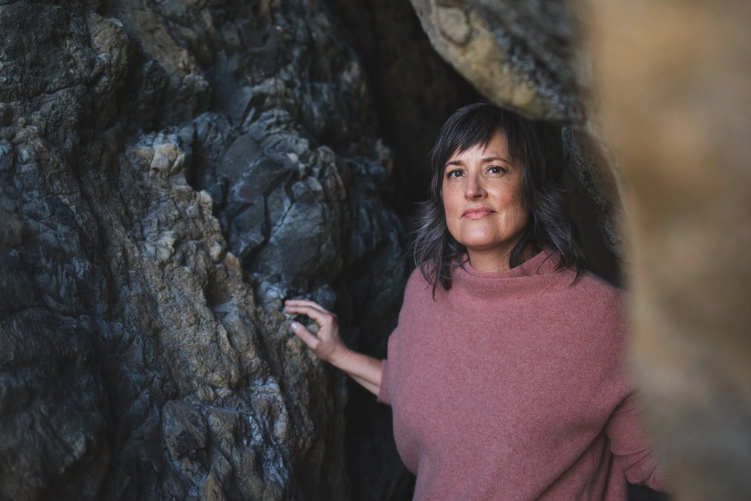 Pema in a pink sweater standing near rocky terrain, looking into the distance.