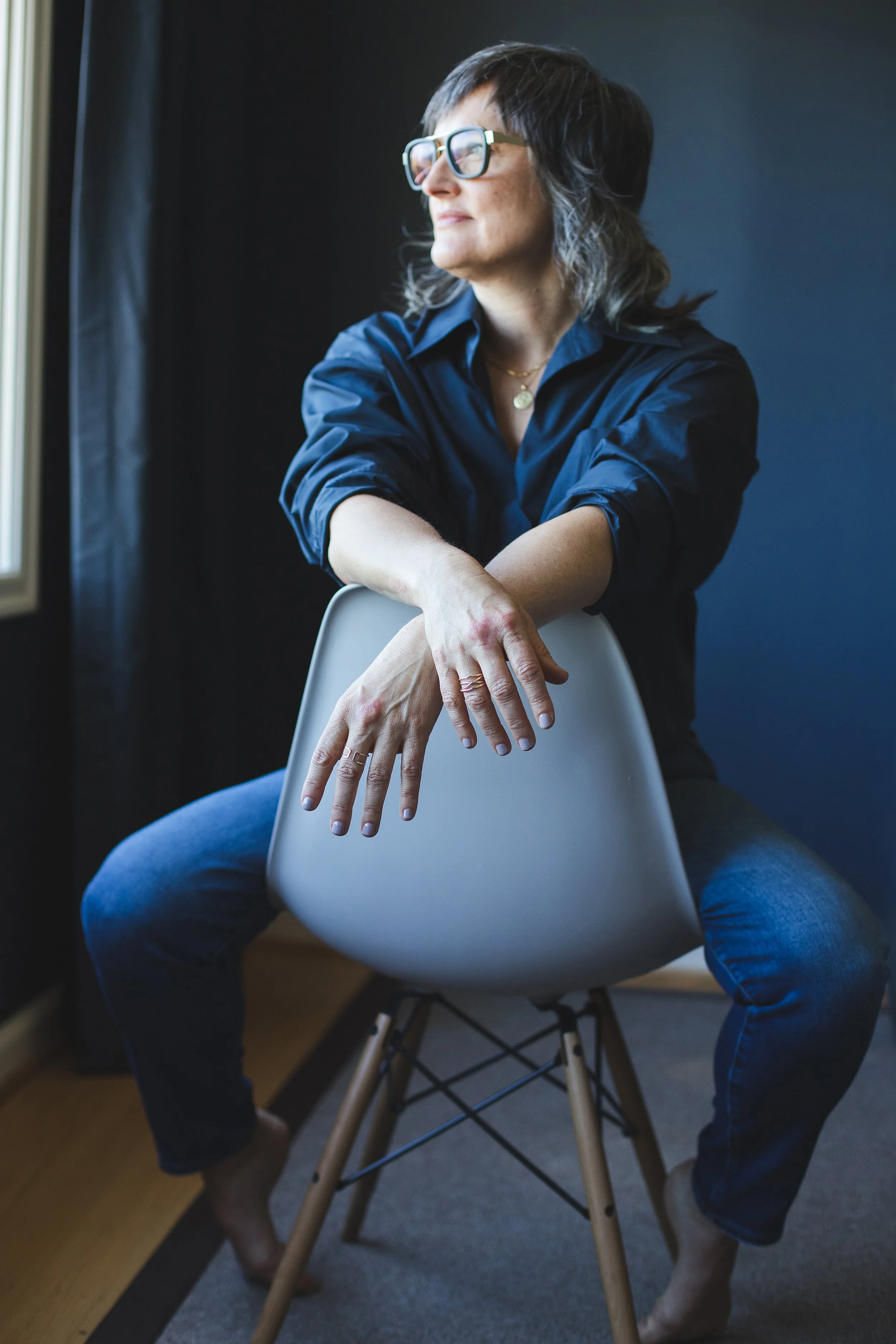 Pema wearing a blue shirt, sitting backwards on a gray chair, looking out the window.