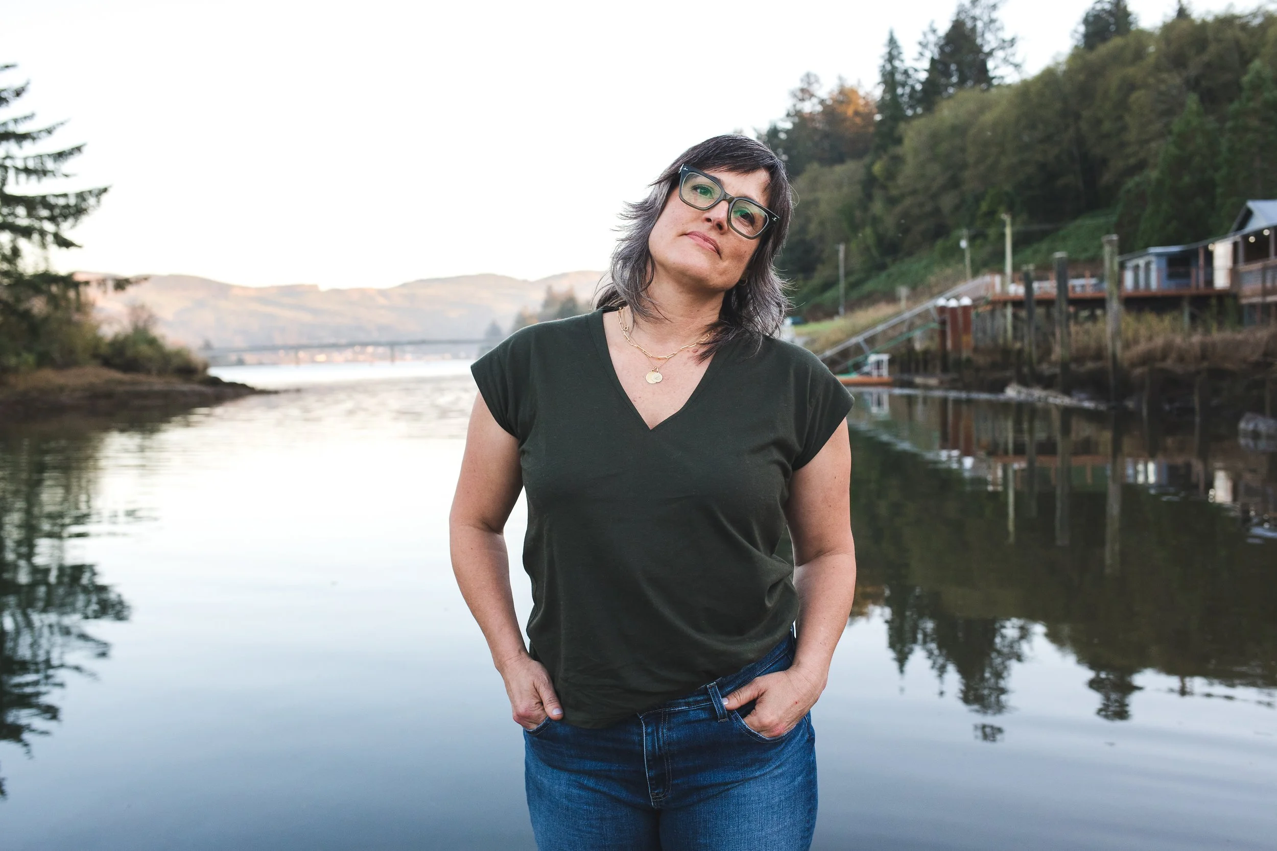 Pema standing near a body of water with trees and houses in the background.