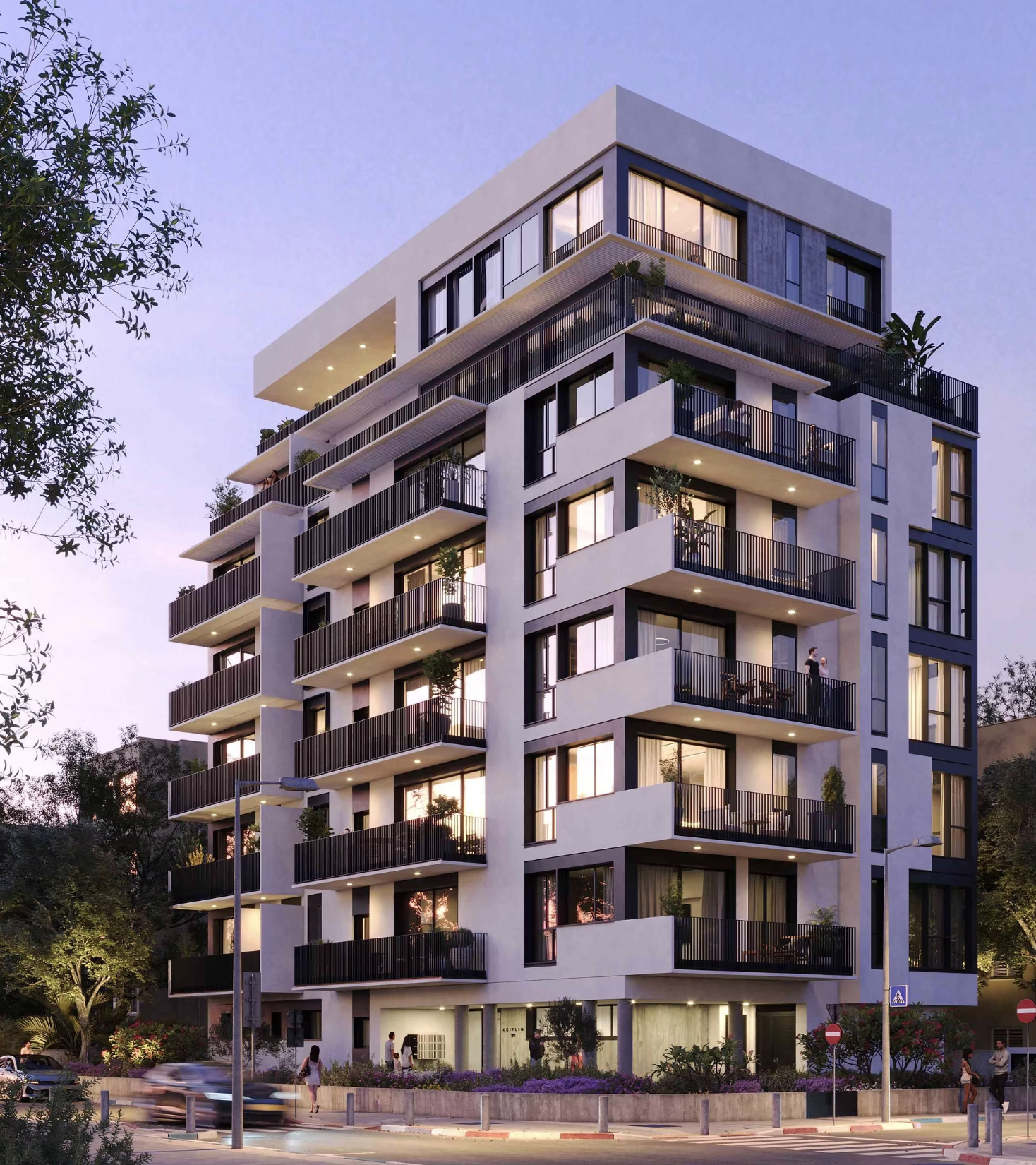A modern multi-story apartment building with balconies, illuminated from within, with trees and street lighting in the foreground during twilight.