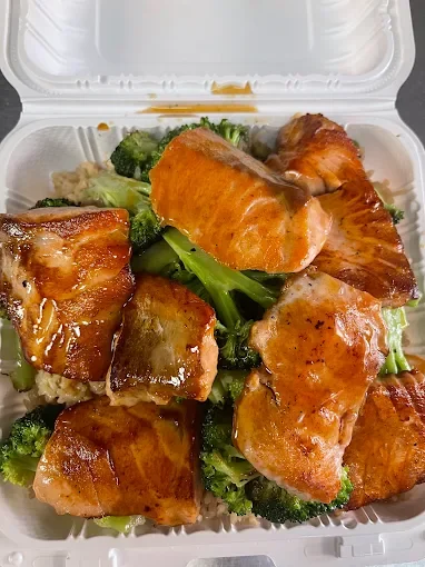 Salmon and bacon pieces served over broccoli and rice in a takeout container.