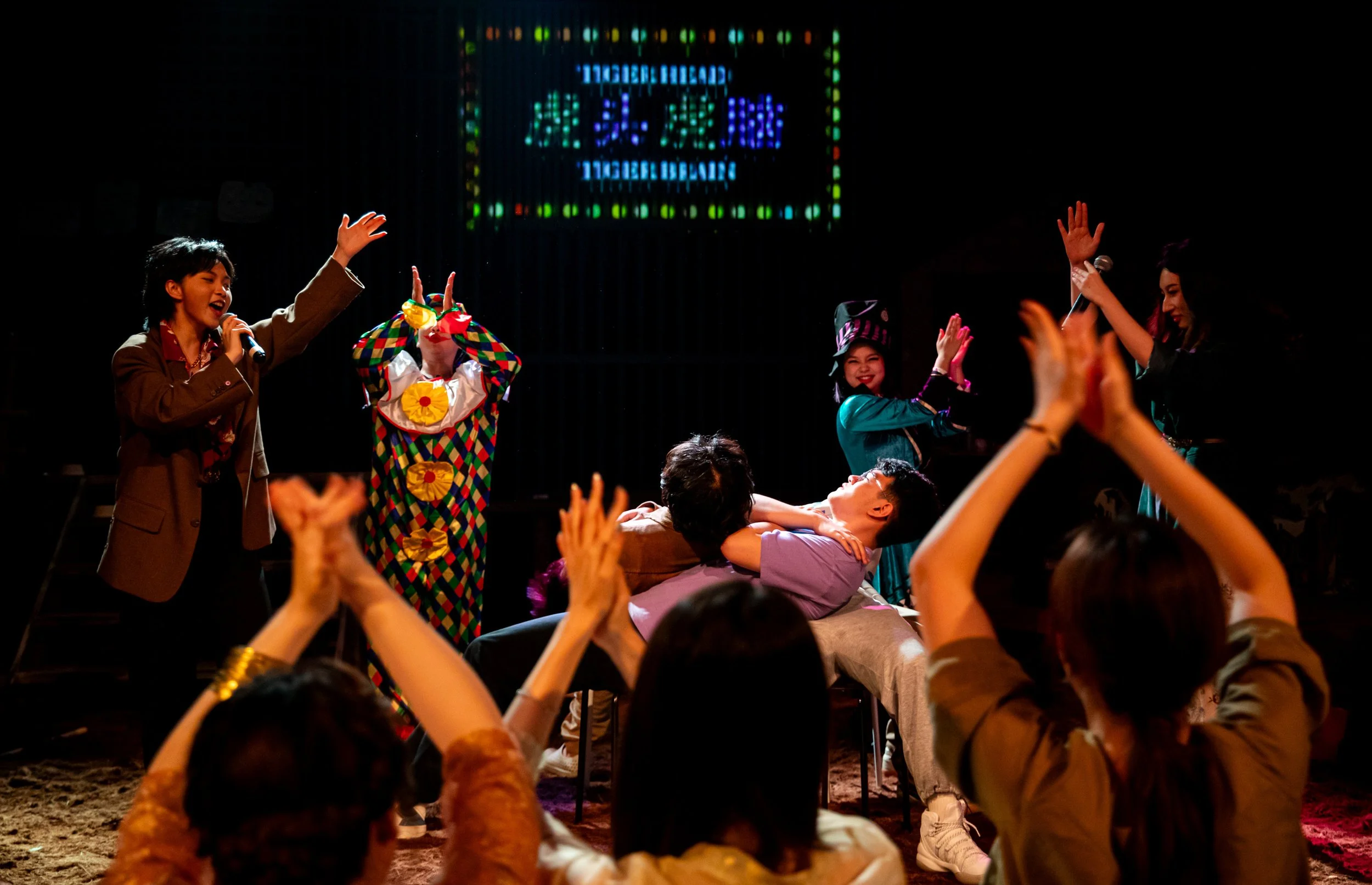 People performing and singing on stage at a lively event with an audience in attendance.