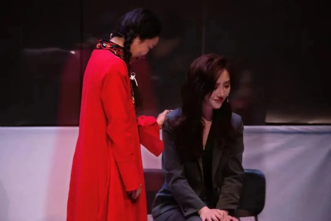 Two women are in a conversation, one standing and the other sitting, in a modern indoor setting.