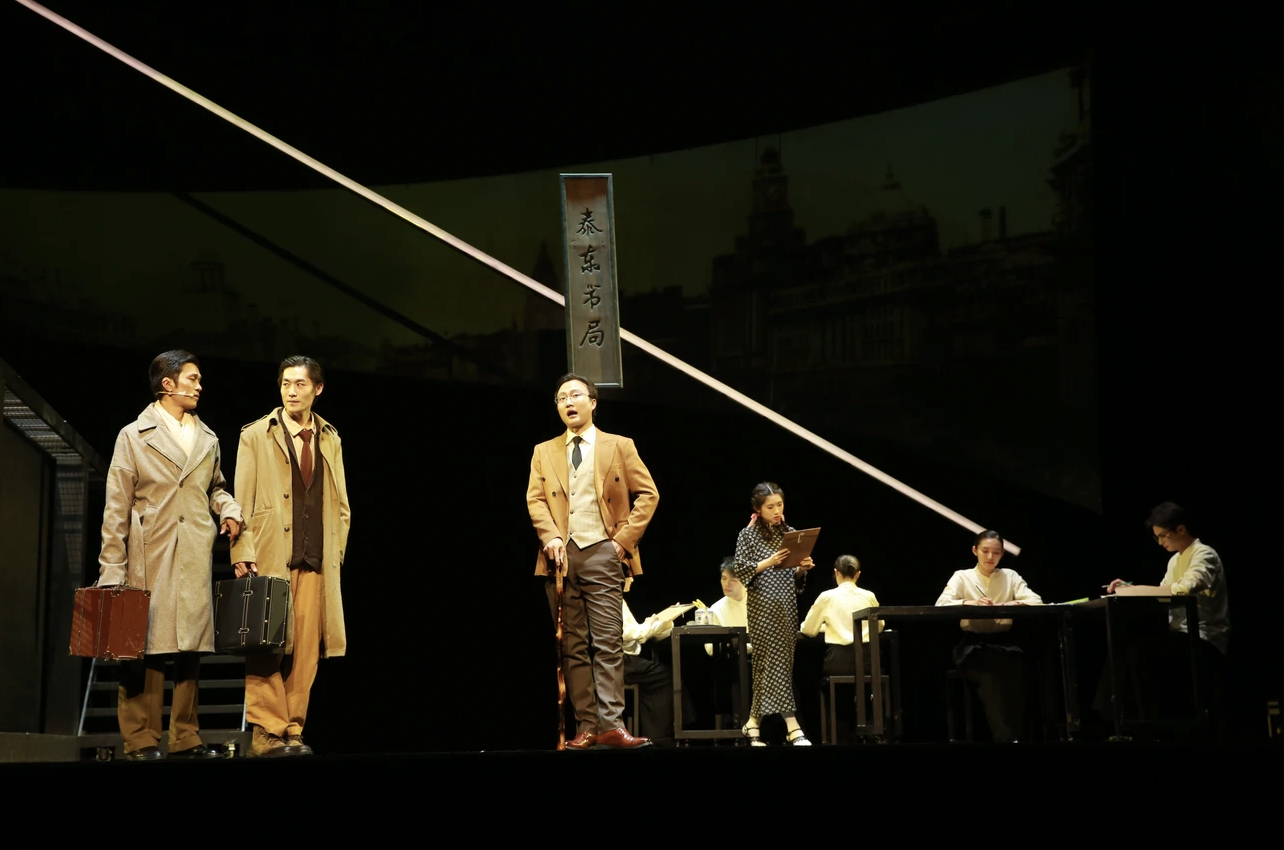Theater scene with actors in vintage costumes and women at desks reading or writing, set against a dark background with a hanging sign in Asian characters.