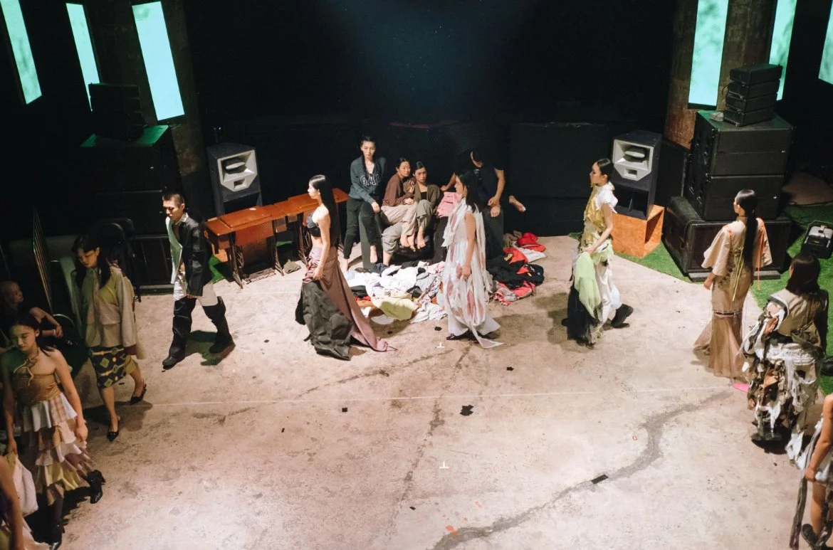 Theater stage with actors preparing backstage, dressed in costumes, with scattered clothes and equipment around.