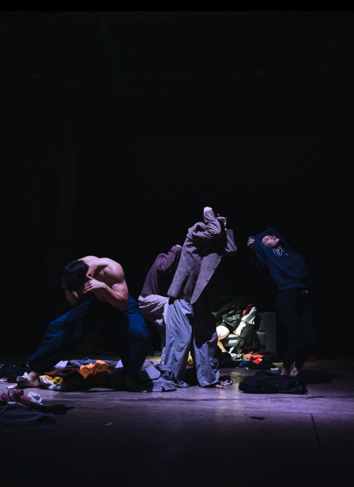 Three people on stage in dramatic poses, surrounded by scattered clothes and personal items, with a dark background.