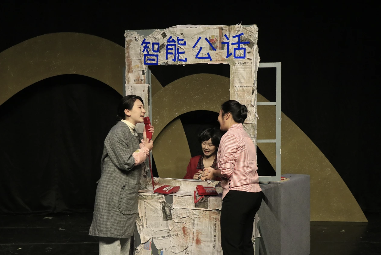 Three women interacting at a newsstand with a sign that says 'Intelligent Public Talk' in Chinese. Two women are standing, one woman is behind the counter.