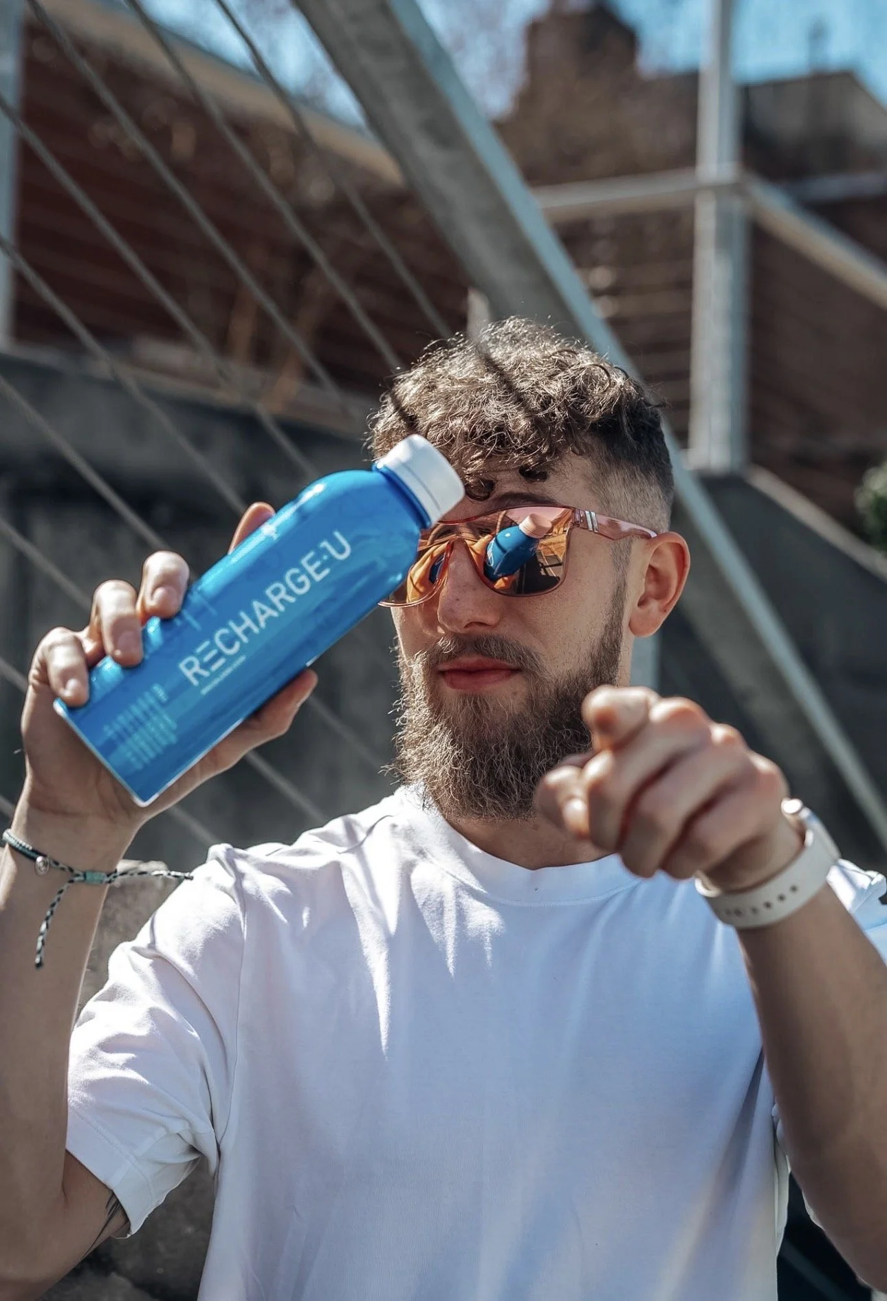 A man with sunglasses and a beard holding a blue rechargeable battery in an outdoor setting.