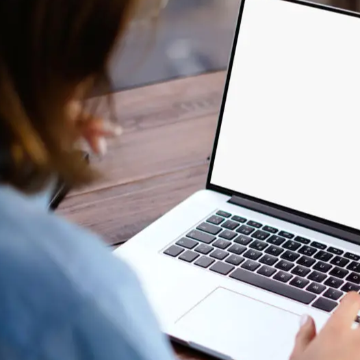 Person using a laptop with a blank white screen at a wooden table.