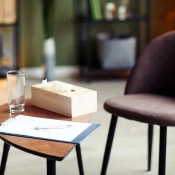 A glass of water, a tissue box, a pen on a notepad, a small table, and a purple upholstered chair in a cozy room.