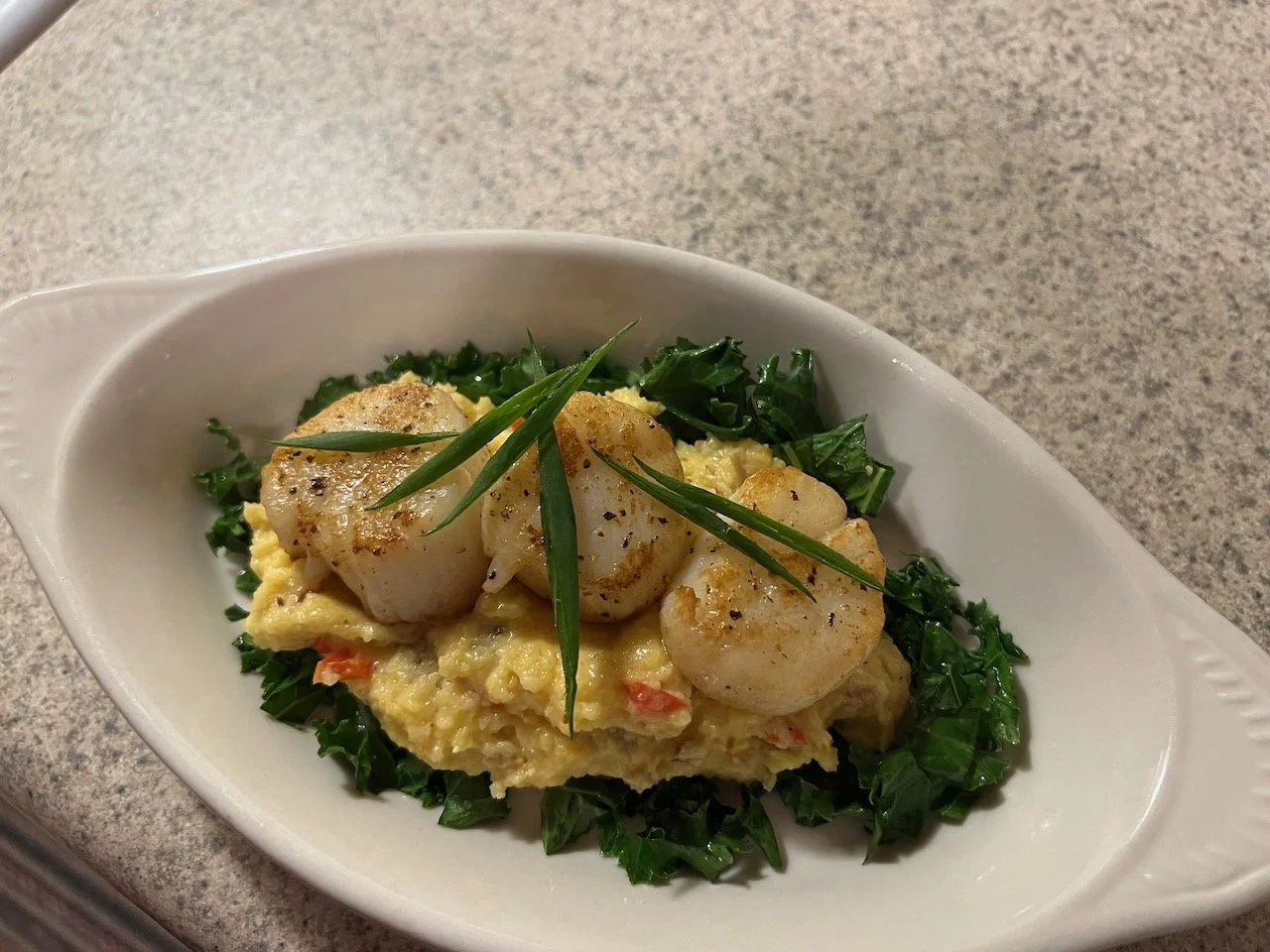 Scallops served on creamy mashed potatoes with chopped greens and garnished with chives.