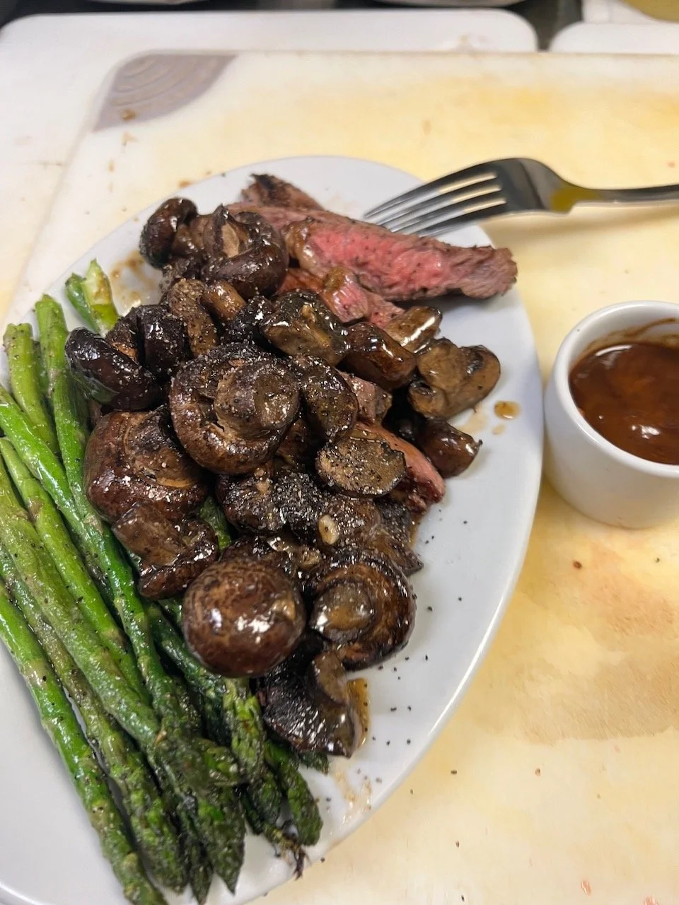 Cooked steak with sautéed mushrooms, green beans, and a small cup of brown gravy.
