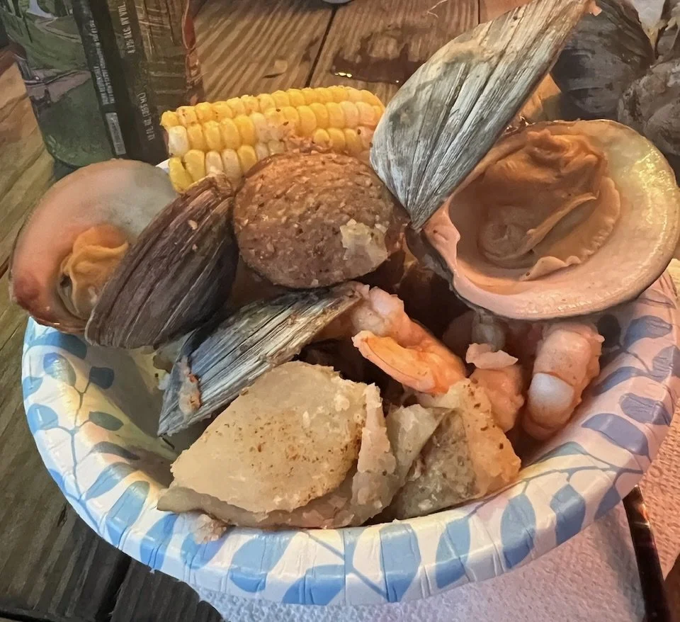 Seafood platter with clams, crab, fish, corn on the cob, and hushpuppies in a paper boat