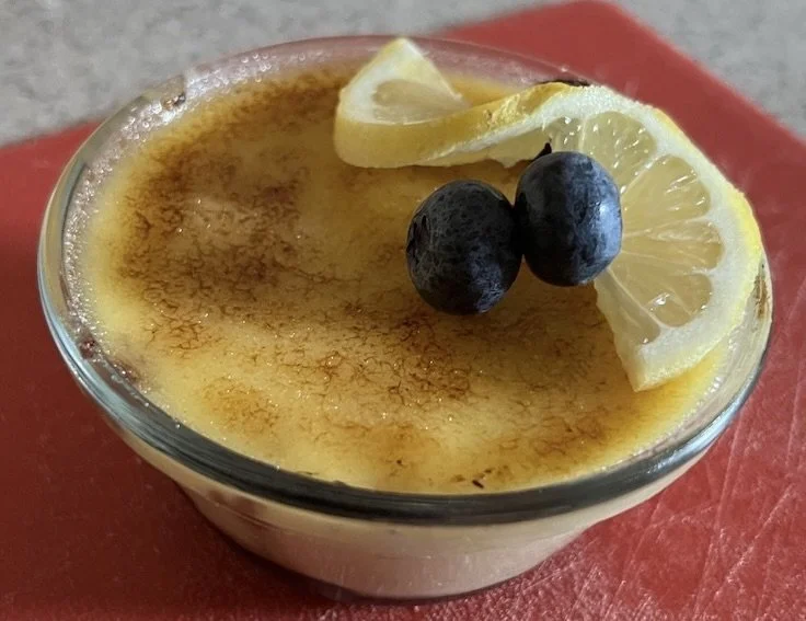 A dessert in a glass bowl with a caramelized sugar top, garnished with lemon slices and blueberries.