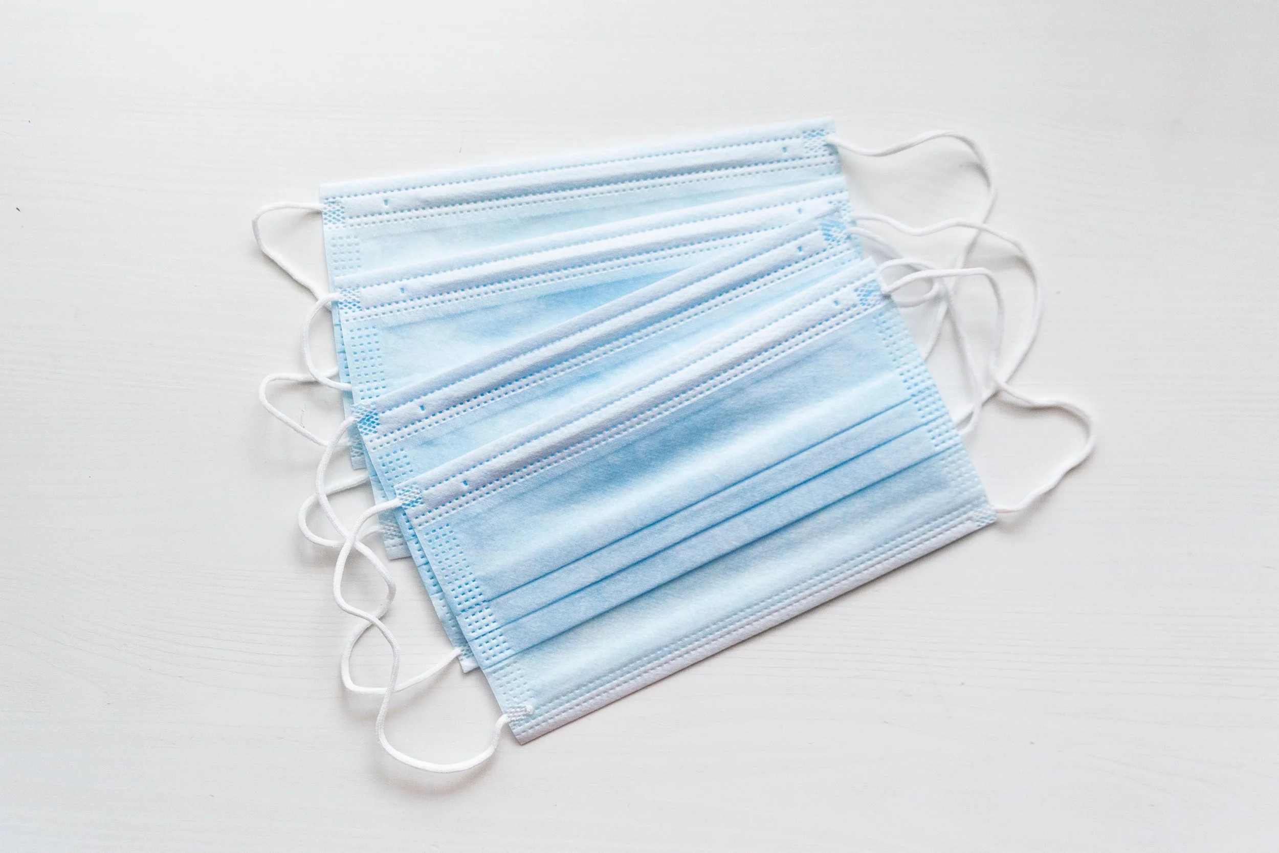 Stack of blue disposable medical face masks on a white surface.