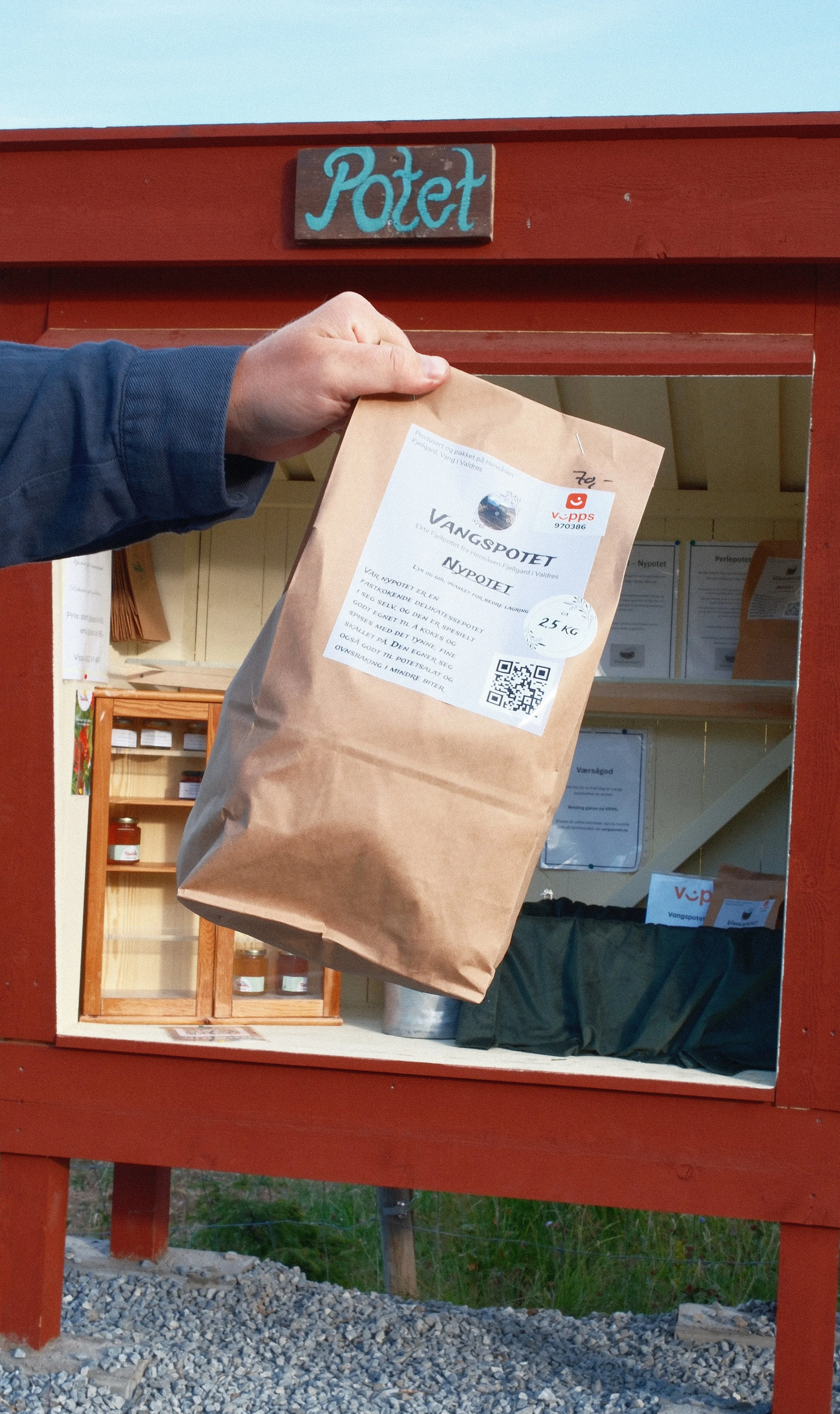 En person henger en pakkelapp med informasjon om en 25 kg fangst på en utendørs postkasse merket 'Potet'. Postkassen er malt rød.