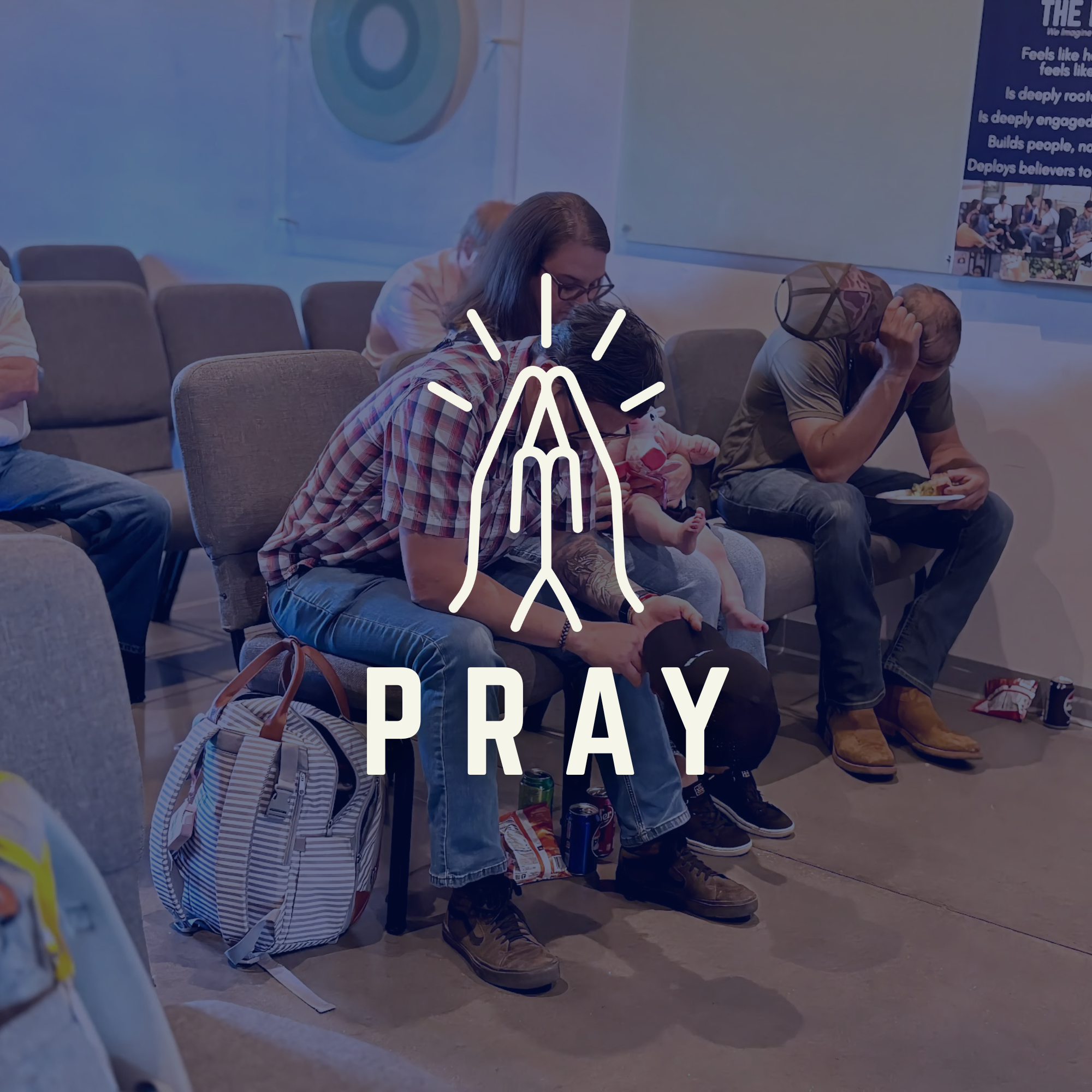 People sitting on chairs in a church, praying with their heads bowed, some with hands clasped and some holding their heads. The environment suggests a church setting with a blue banner on the wall with religious text and image.
