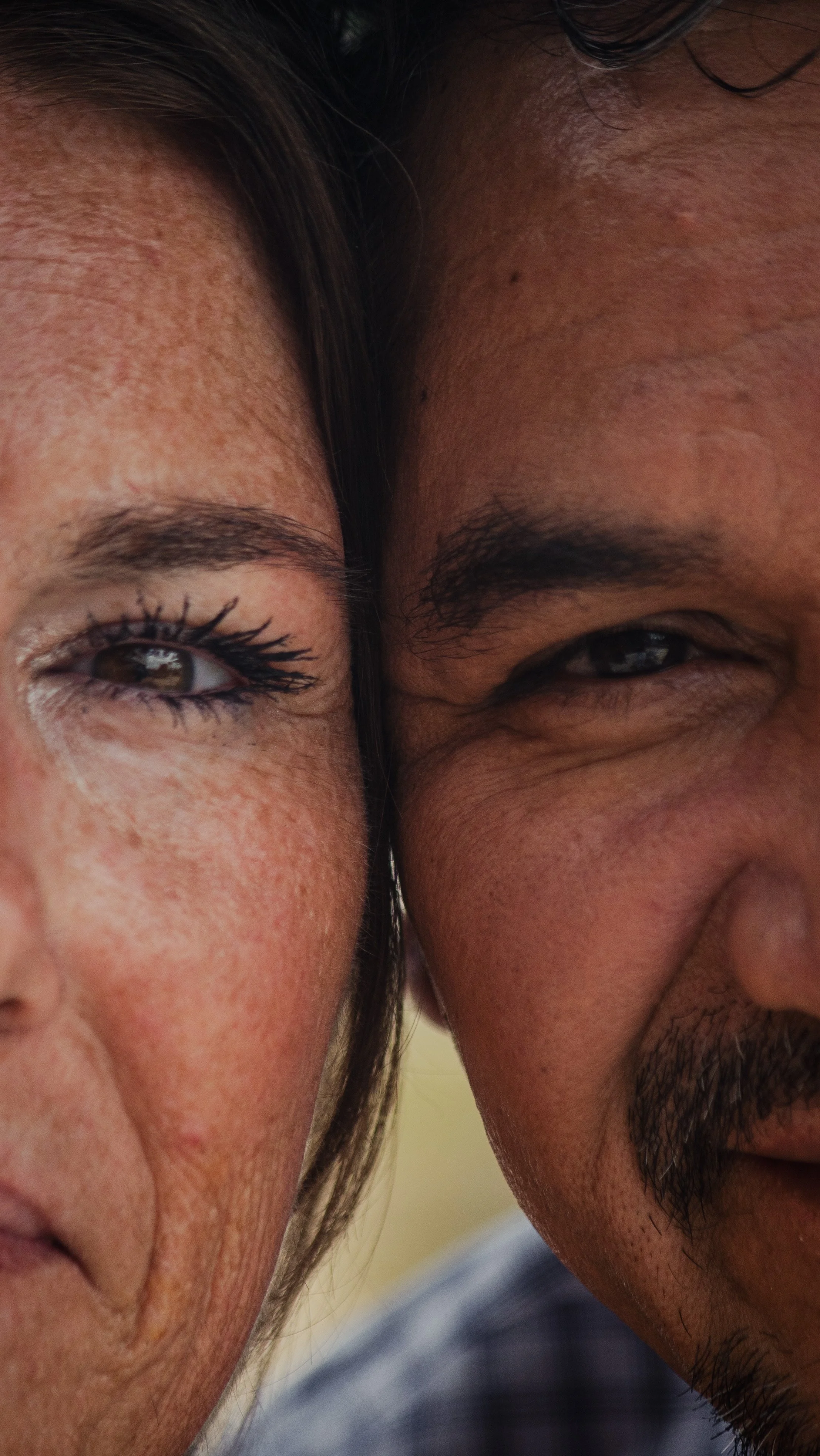Close-up of a woman and a man with their faces touching, showing eyes and upper cheeks.