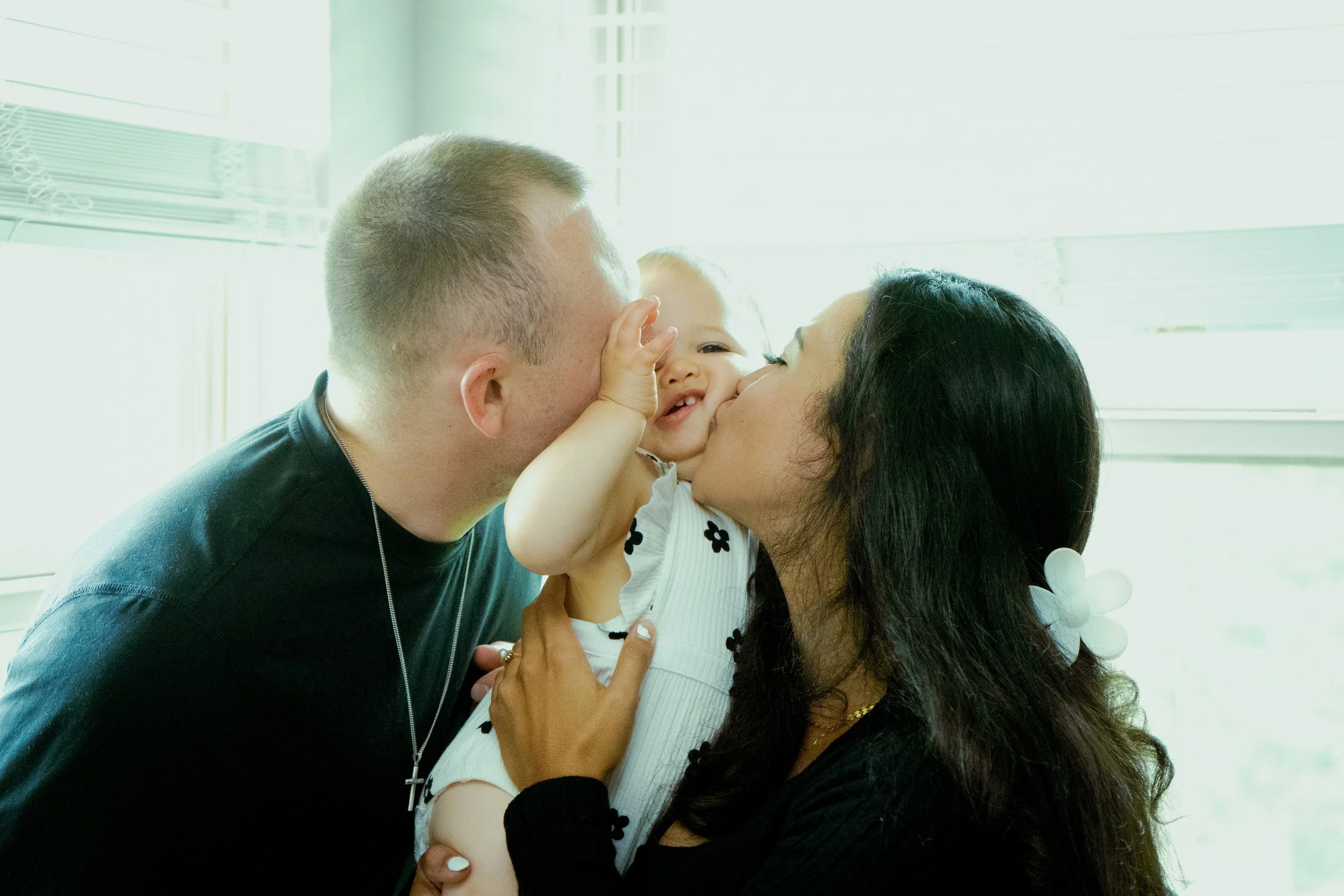 A family of three, a man, a woman, and a young girl, sharing a loving moment with the girl touching the man's face and all smiling.