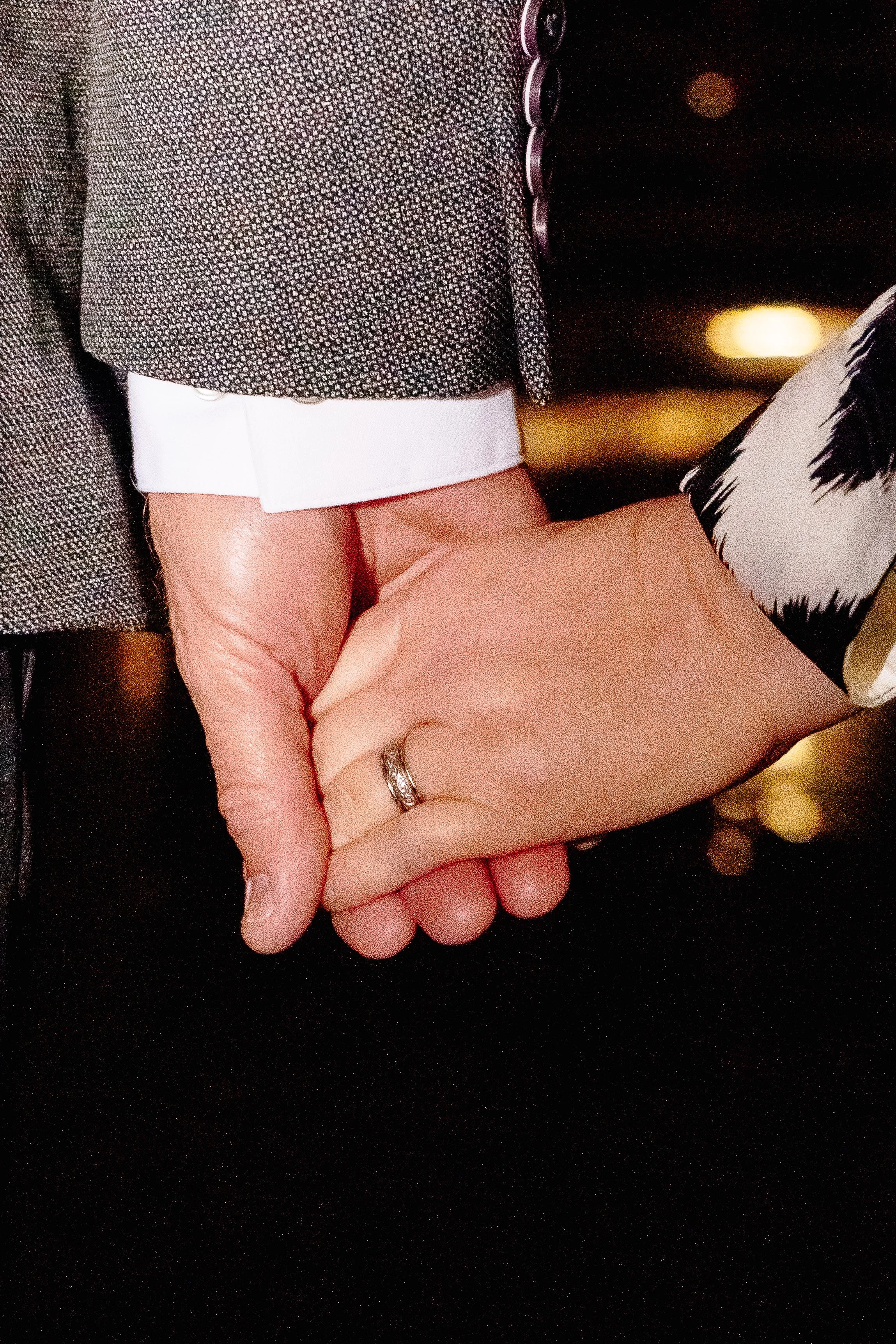 Close-up of a person in business attire holding hands with another person, focusing on the handshake. The person wearing a patterned blazer and white shirt is grasping the hand of another individual, with a blurred background.
