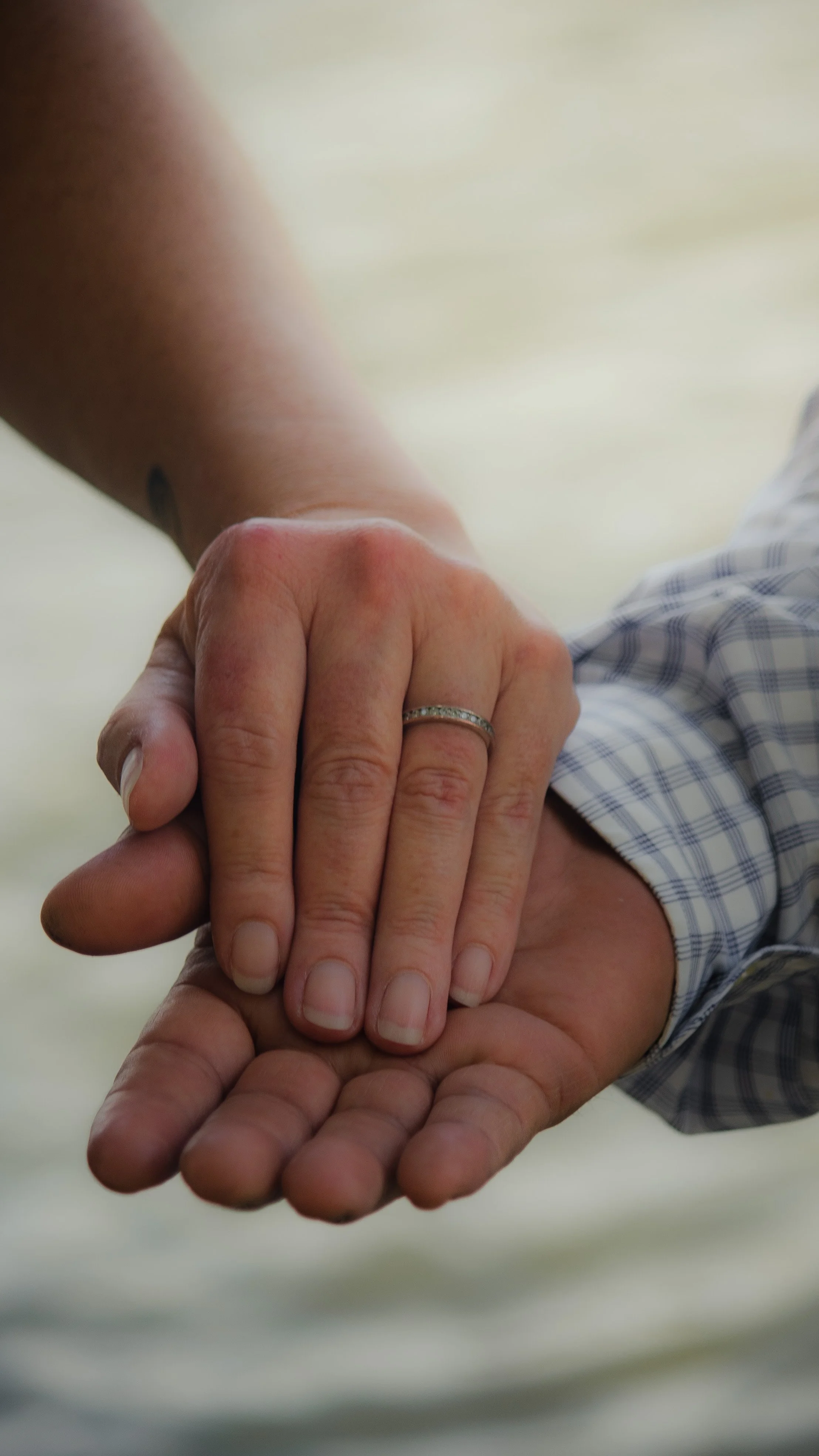 Two people holding hands, including a woman with a wedding ring and man with a watch, with a blurred background.