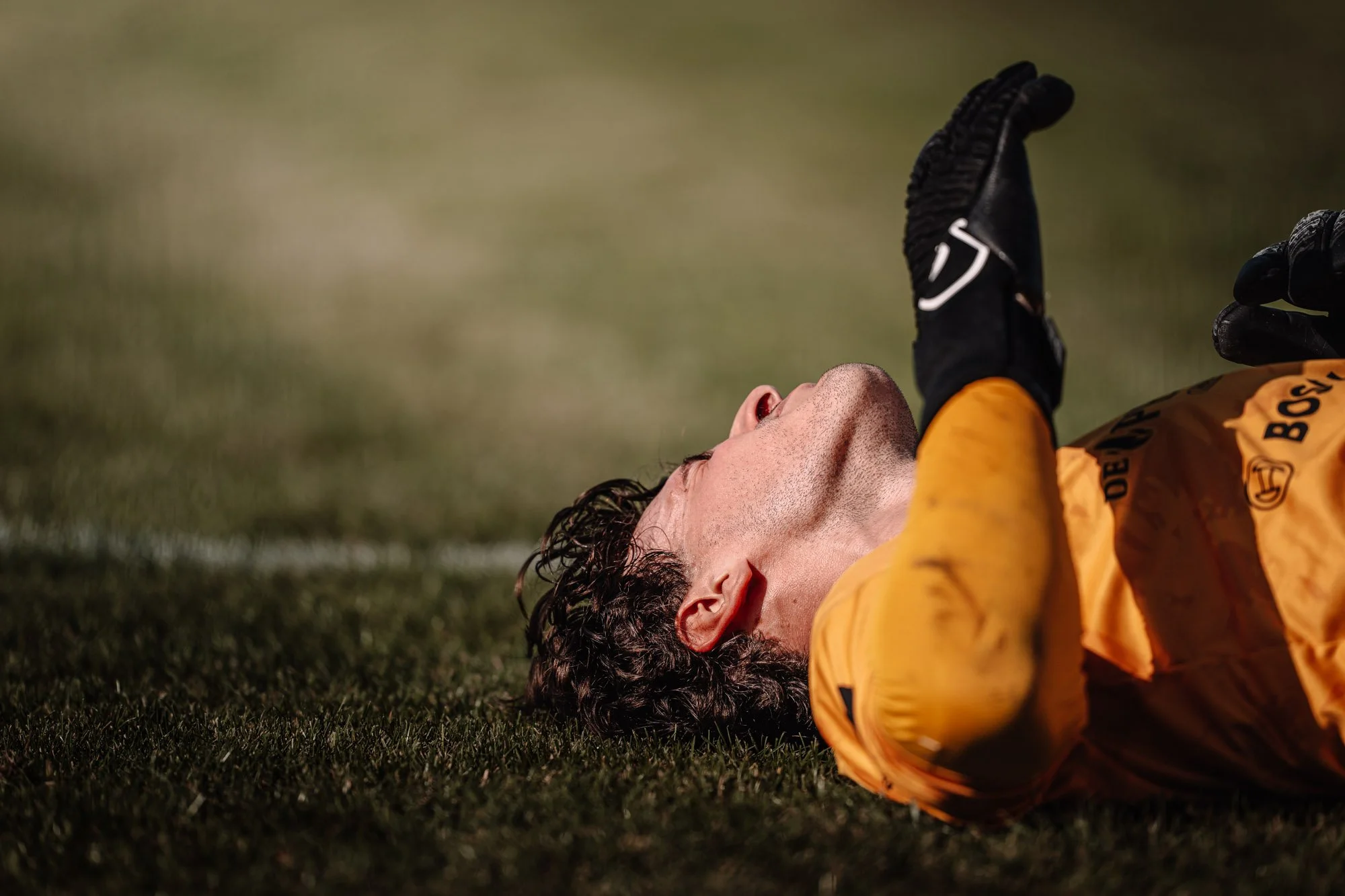 Amper een voetbalspeler ligt op zijn rug op het grasveld met een hand omhoog, mogelijk na een val of blessure.