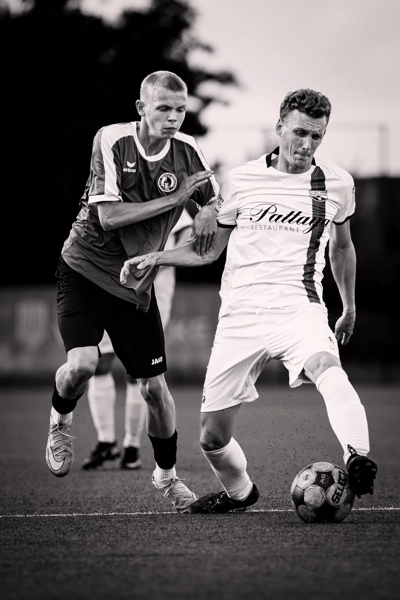Twee voetbalspelers in actie, één met een bal, op een grasveld, zwart-wijn foto