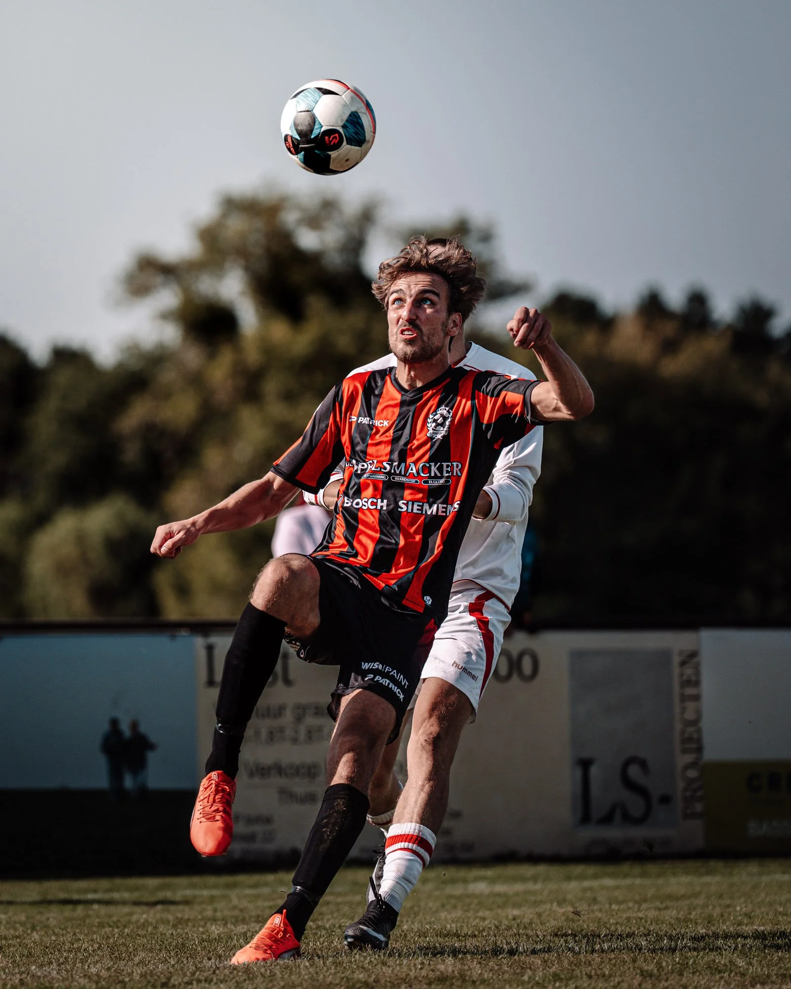 Een vrouwelijke voetballer in een zwart en rood tenue maakt een kopbal tijdens een wedstrijd.