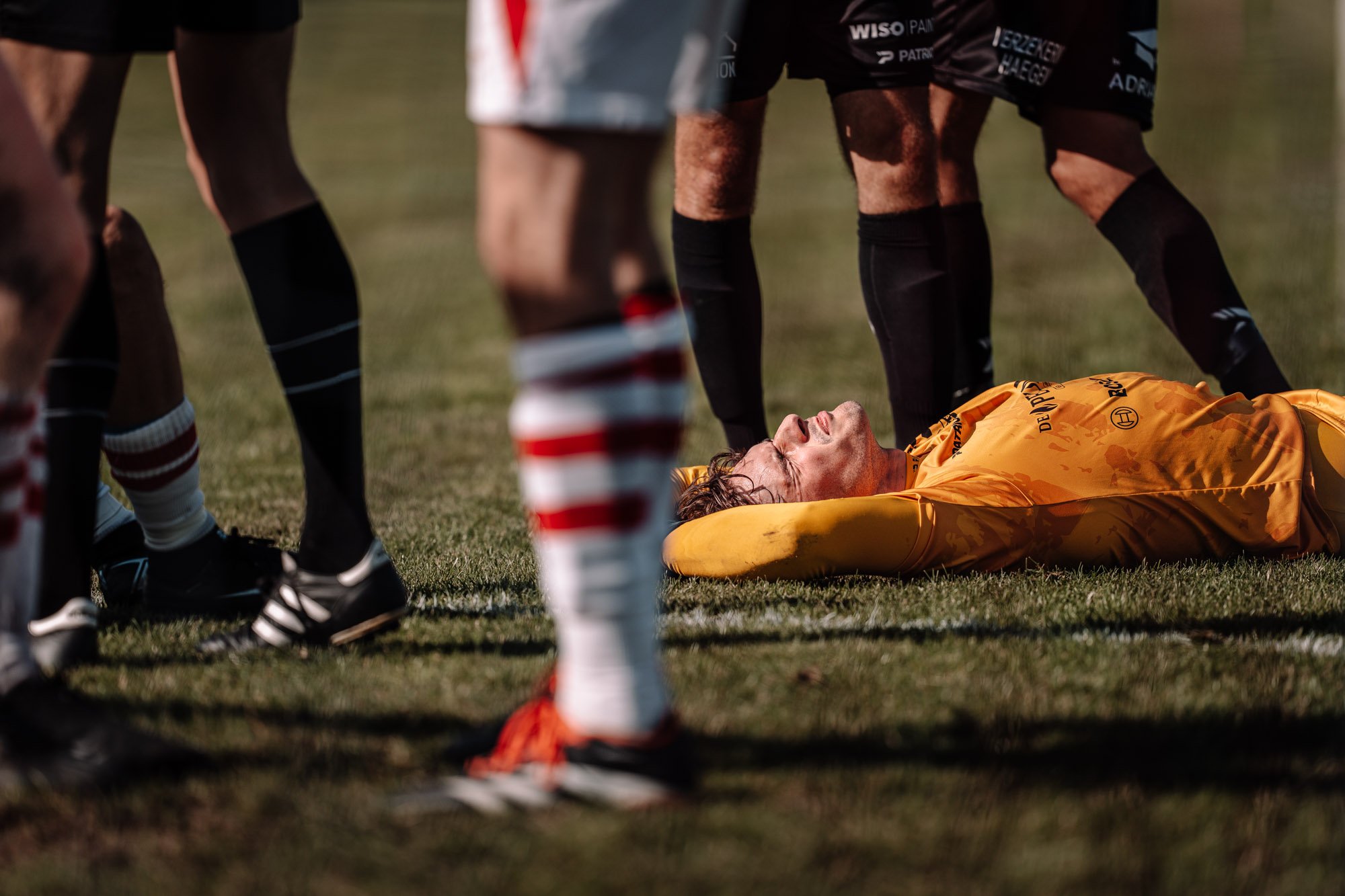 Een speler ligt op de grond tijdens een voetbalwedstrijd, omringd door andere spelers.