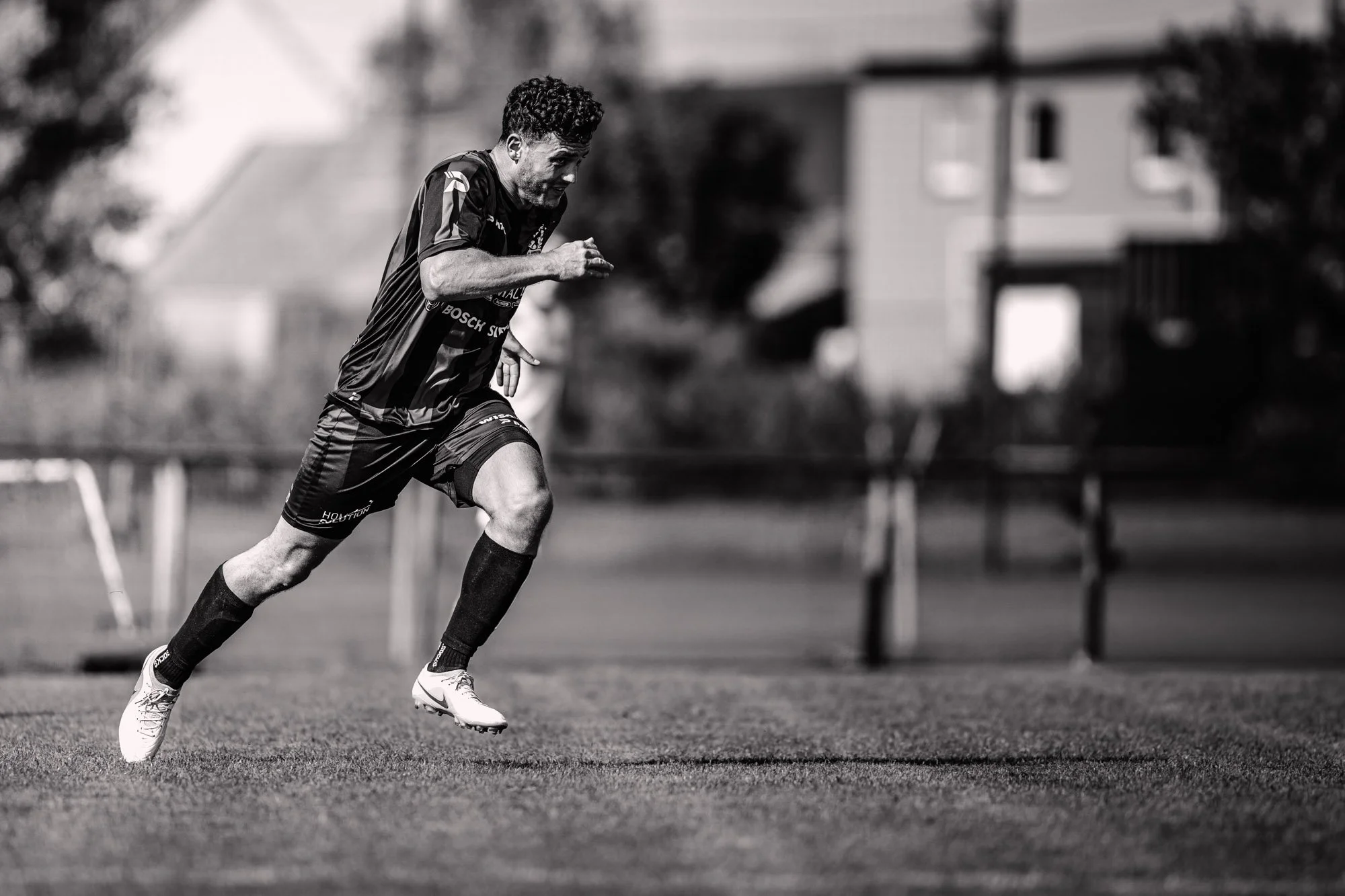 Zwart-wit foto van een man die aan het hardlopen is op een grasveld. Hij draagt sportkleding en spikes, en lijkt zich te concentreren op zijn fysieke inspanning.