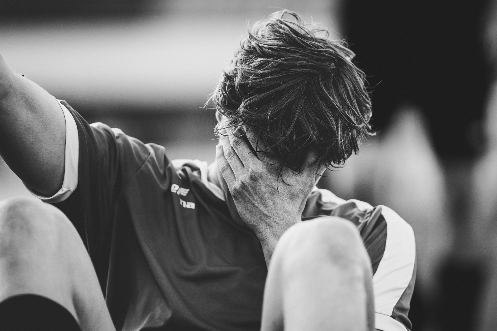 Zwart-wit foto van een sporter die zich verslagen voelt, met hand op het gezicht, mogelijk na een wedstrijd of inspanning.