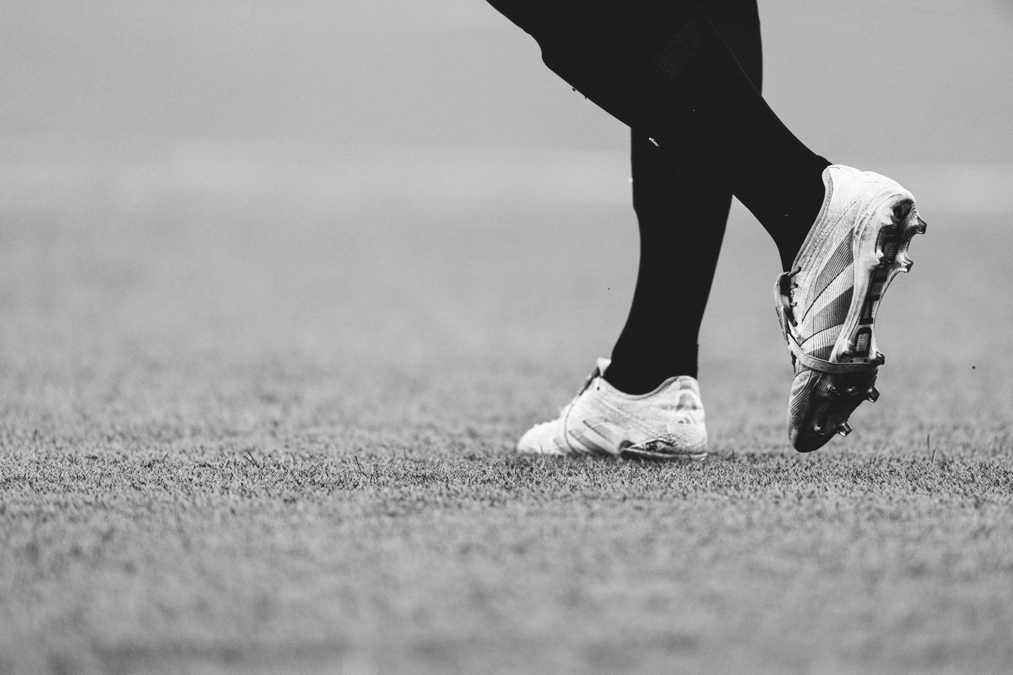 Dichtbij opname van een voetbalspeler die zich voorbereidt op een trap, met focus op zijn schoenen en benen.