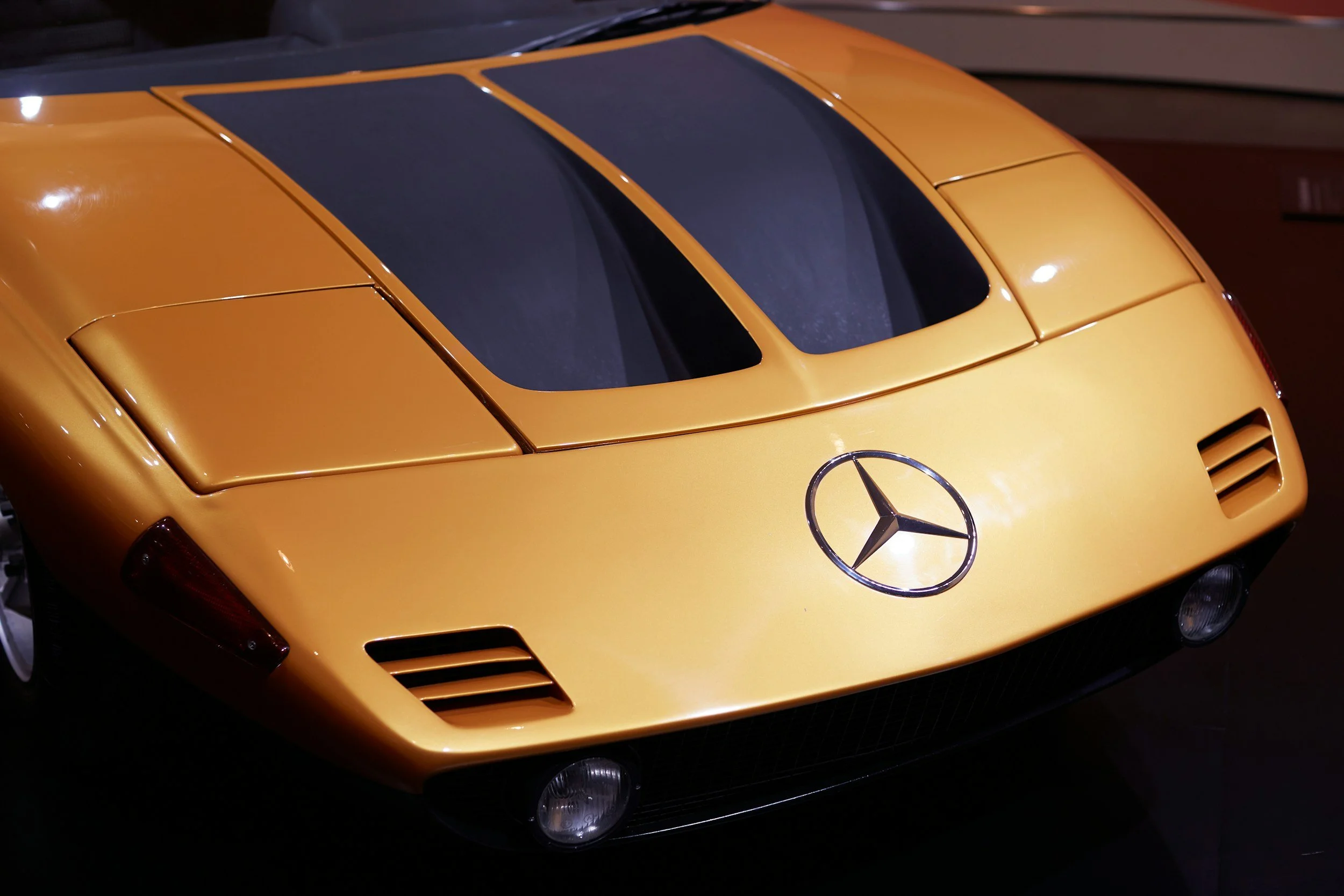 A yellow Mercedes-Benz sports car with a black roof, parked in a dimly lit area.