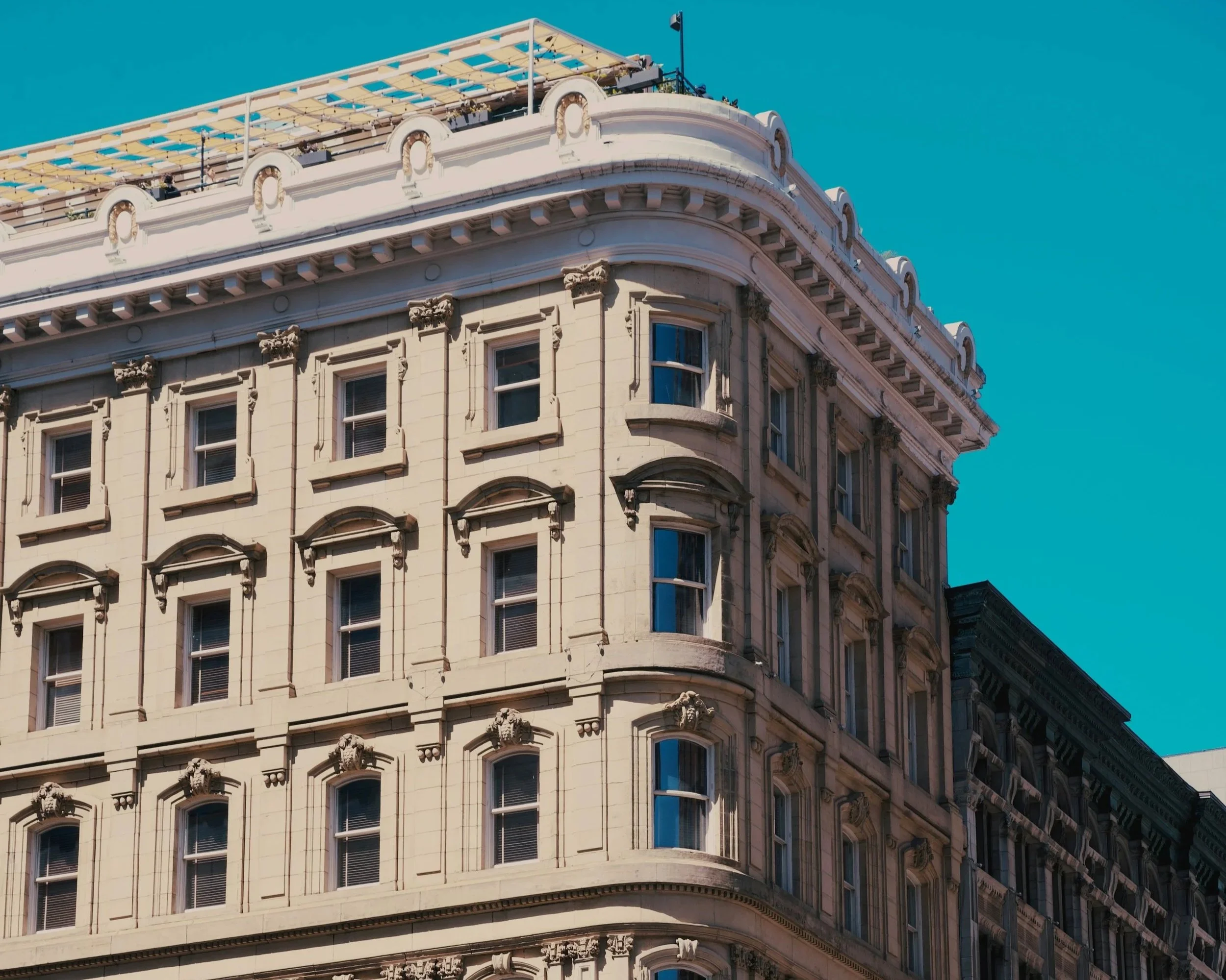 Edificio clásico de varios pisos con ventanas grandes y decoraciones en la fachada, bajo un cielo azul claro.