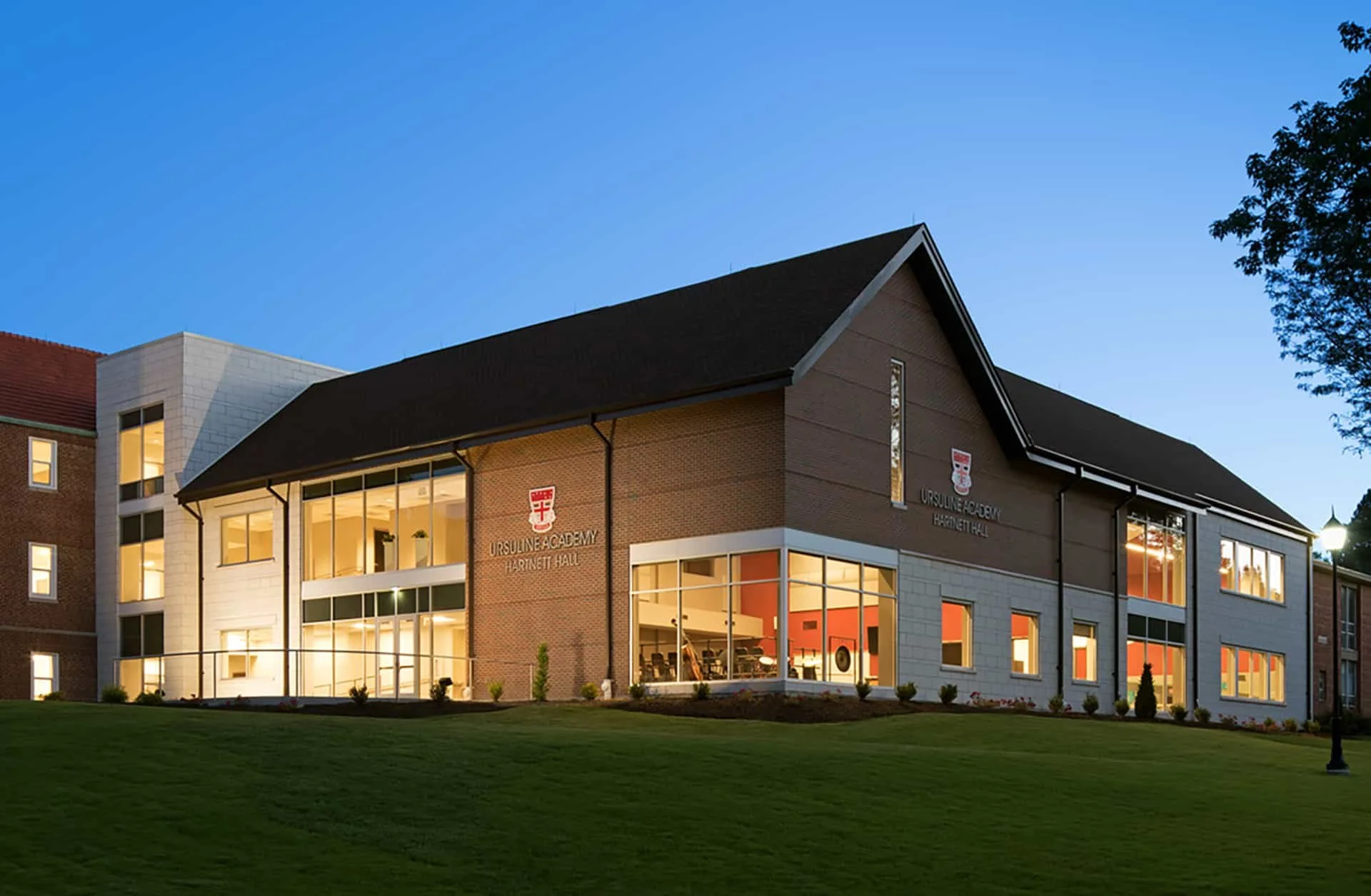 Exterior view of Ursuline Academy Hartnett Hall building at dusk, showcasing modern architecture with large windows and trees in the foreground.