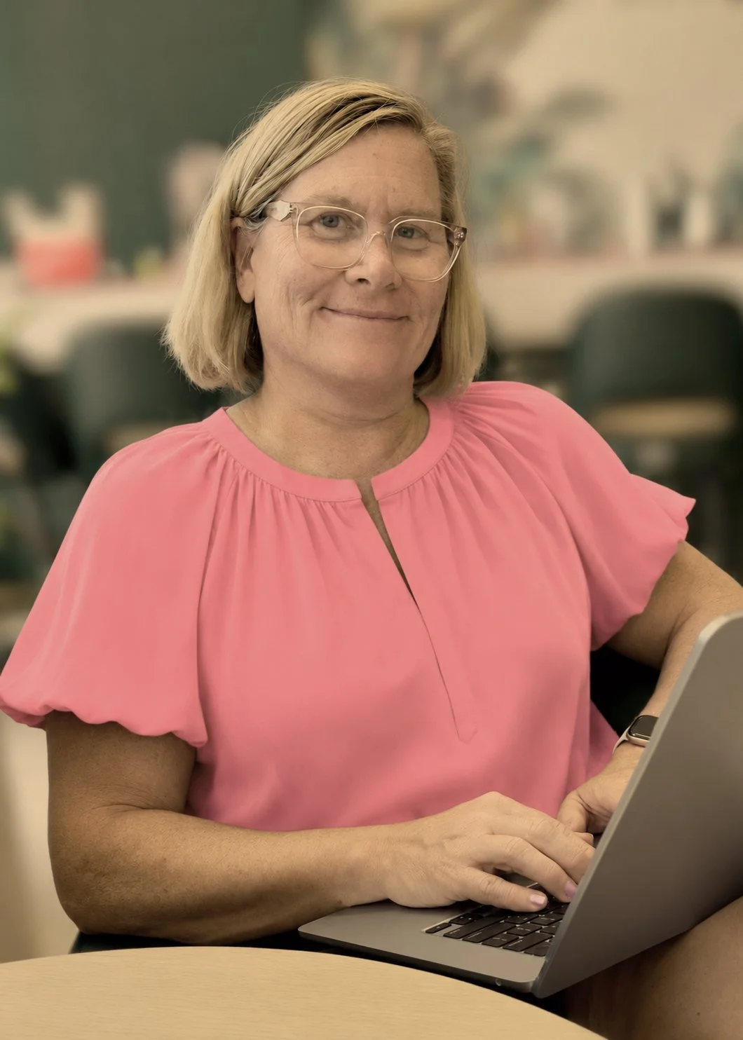 Jen Brooks working at a laptop in a pink blouse.