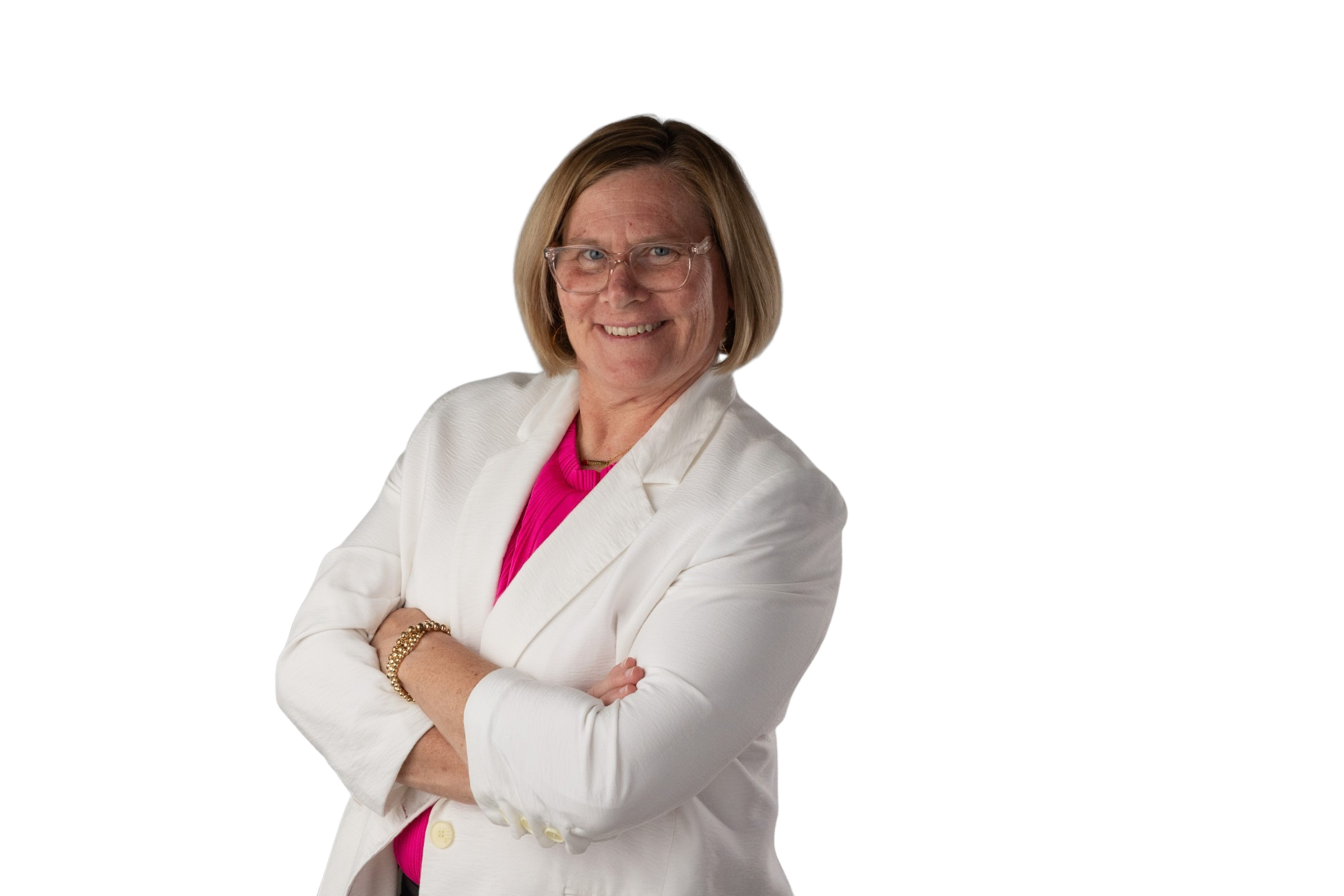 A woman with shoulder-length blond hair, wearing glasses, a white blazer, a pink top, and gold jewelry, smiling and crossing her arms.
