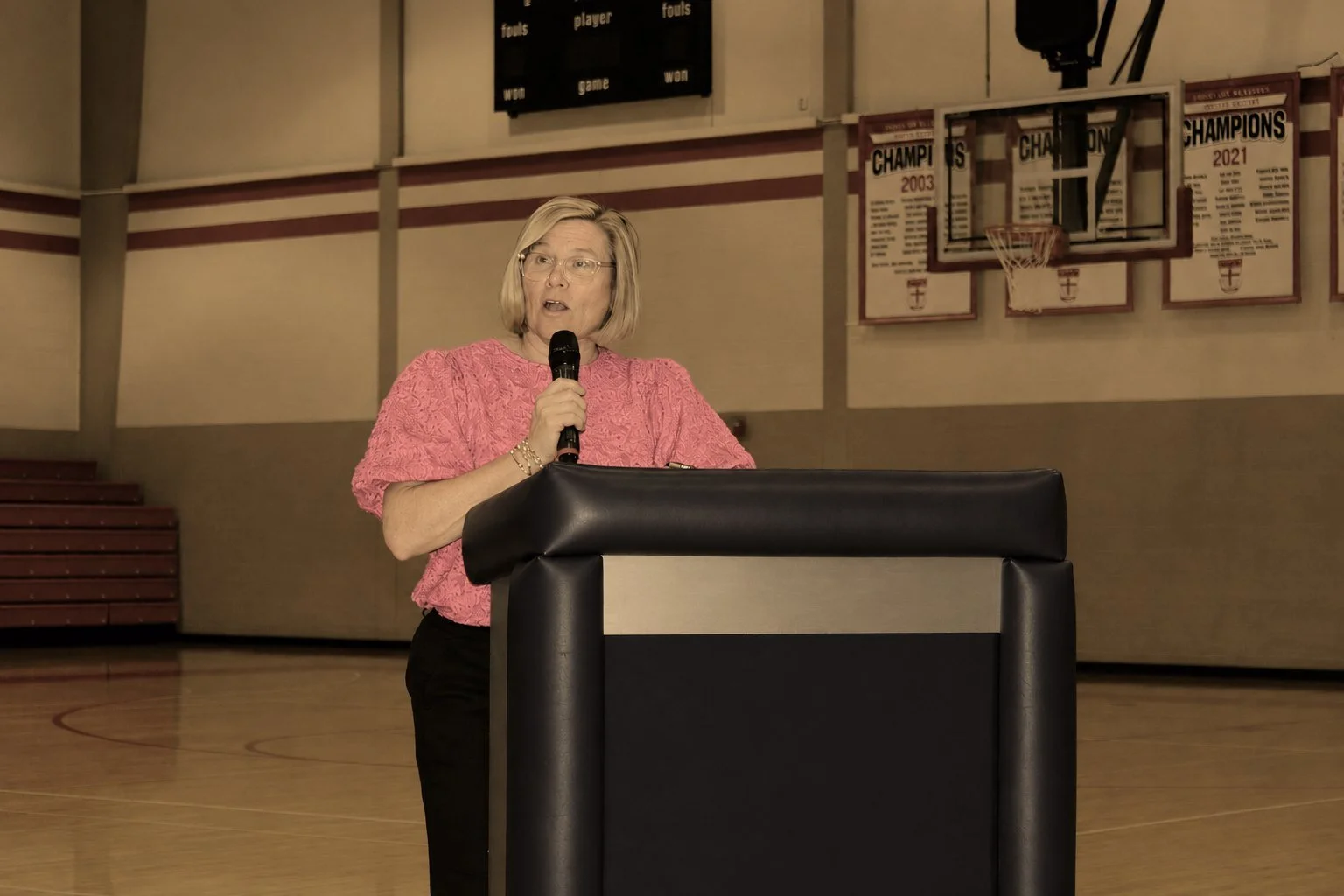Jen Brooks speaking at a podium in a school gymnasium.
