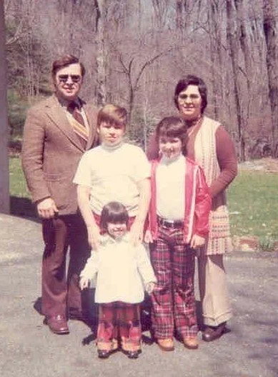 A vintage photograph of a family of five outdoors in a wooded area, with two adults and three children, dressed in 1970s-style clothing.