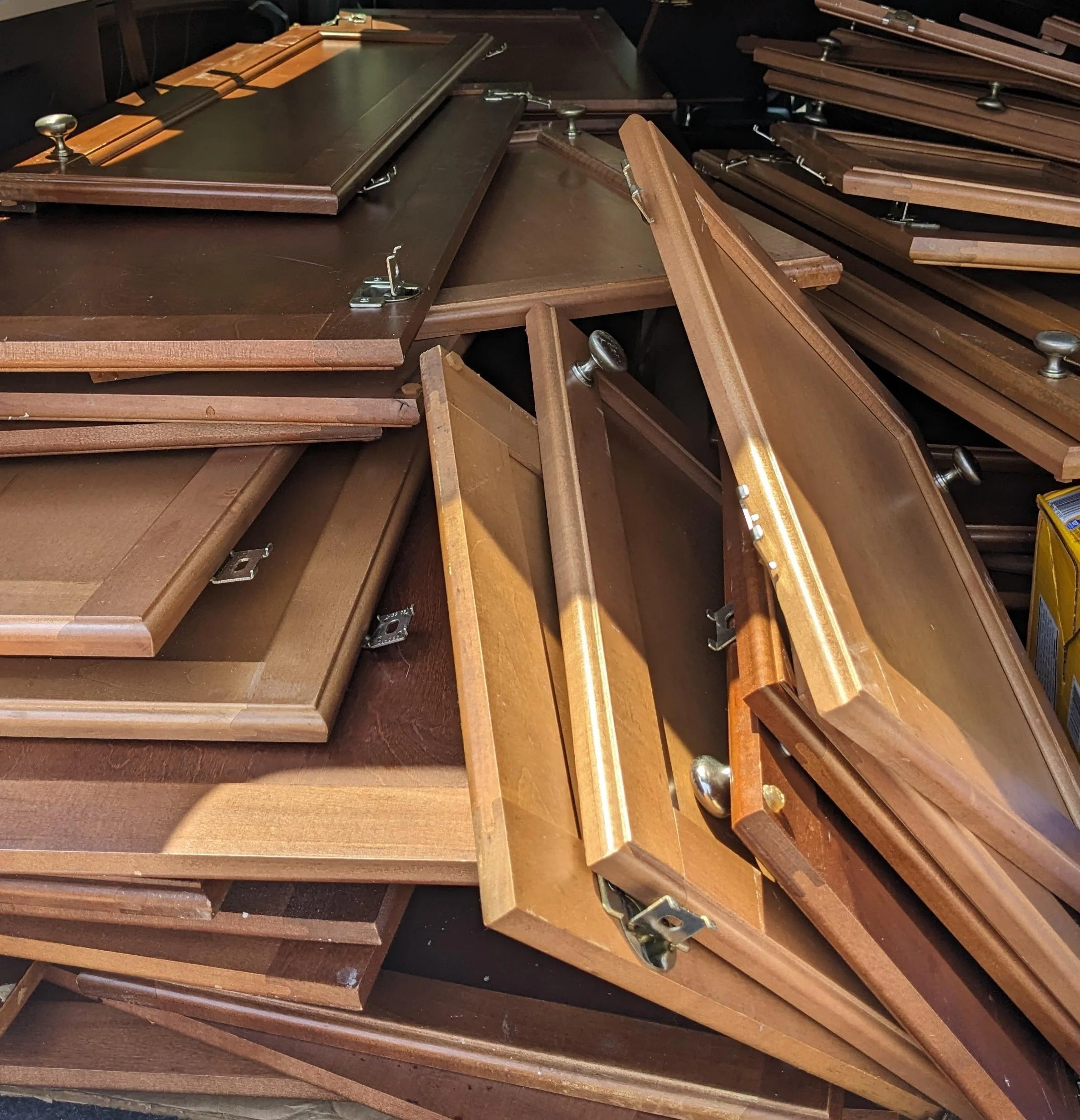 Display of multiple wooden tables or desks stacked together, with some showing metal hinges or framing.
