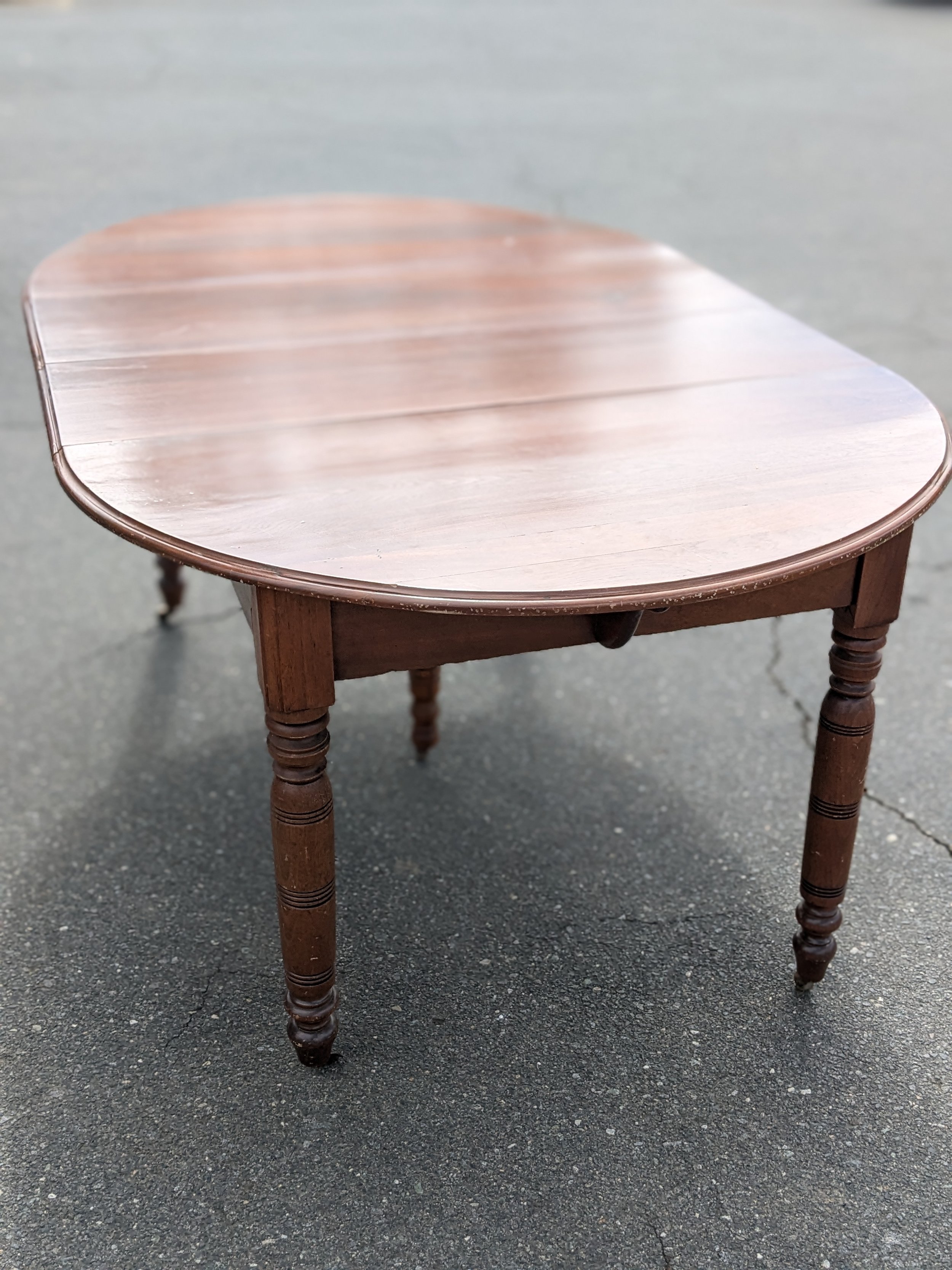 Wooden table with a rounded rectangular top and four turned legs, placed on a paved surface.