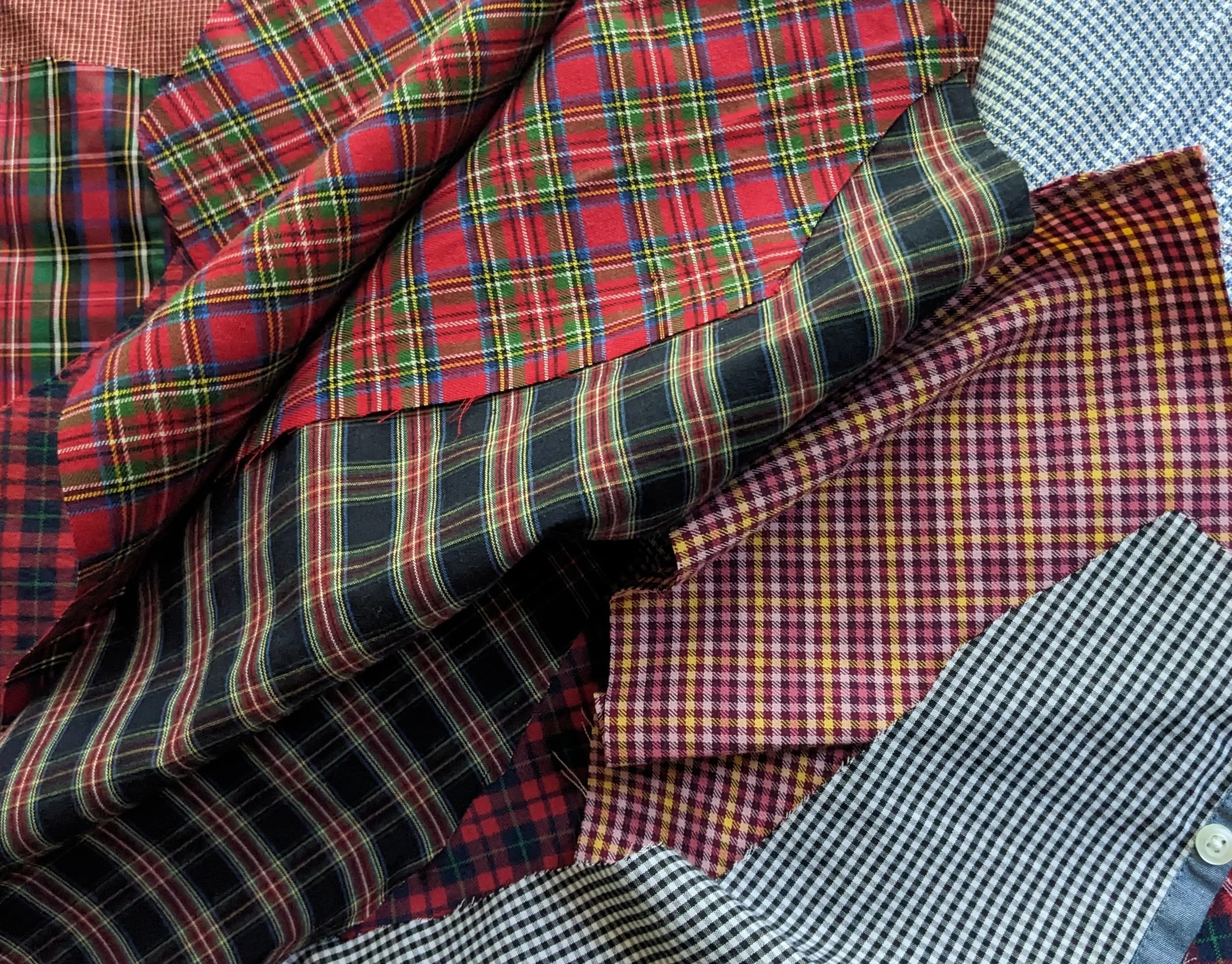 A pile of folded, colorful plaid flannel shirts with various patterns including red, green, blue, yellow, and checkered designs.