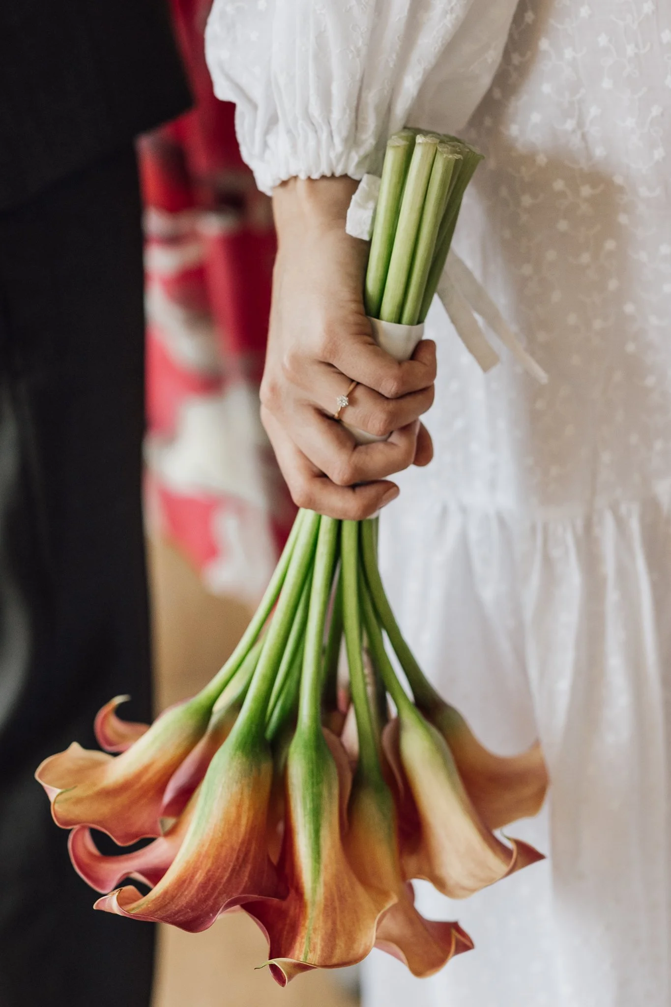 Person, der holder en buket blomster med lange grønne stilke og store, orangefarvede blomster med krøllede lag.