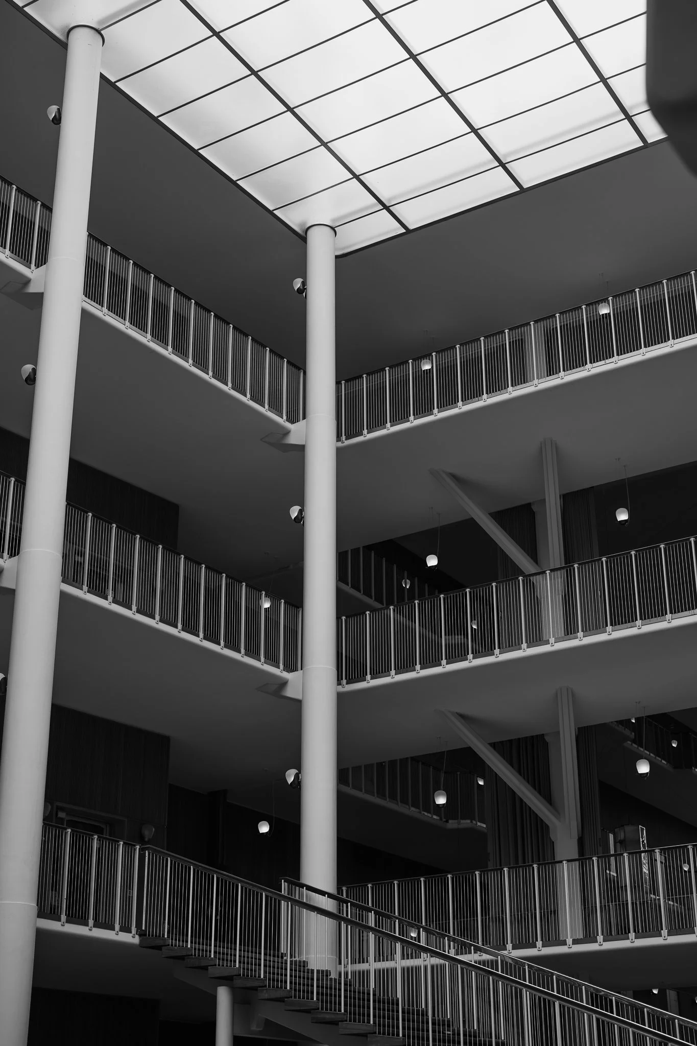 Sort-hvid billede af en modern, todelt udendørs atrium med trapper og gelændere, taget oppefra.