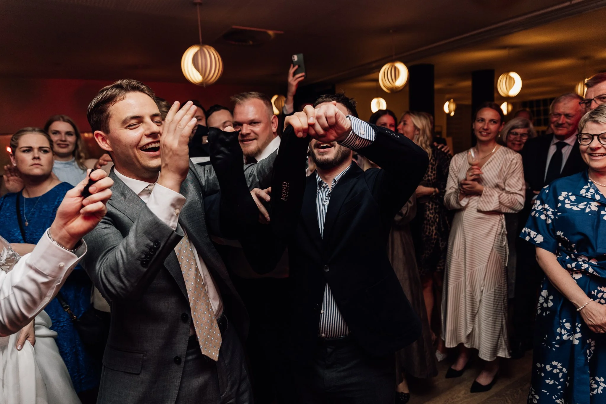 Mennesker danser og hygger sig til en fest i et indendørs lokale med varme belysning.