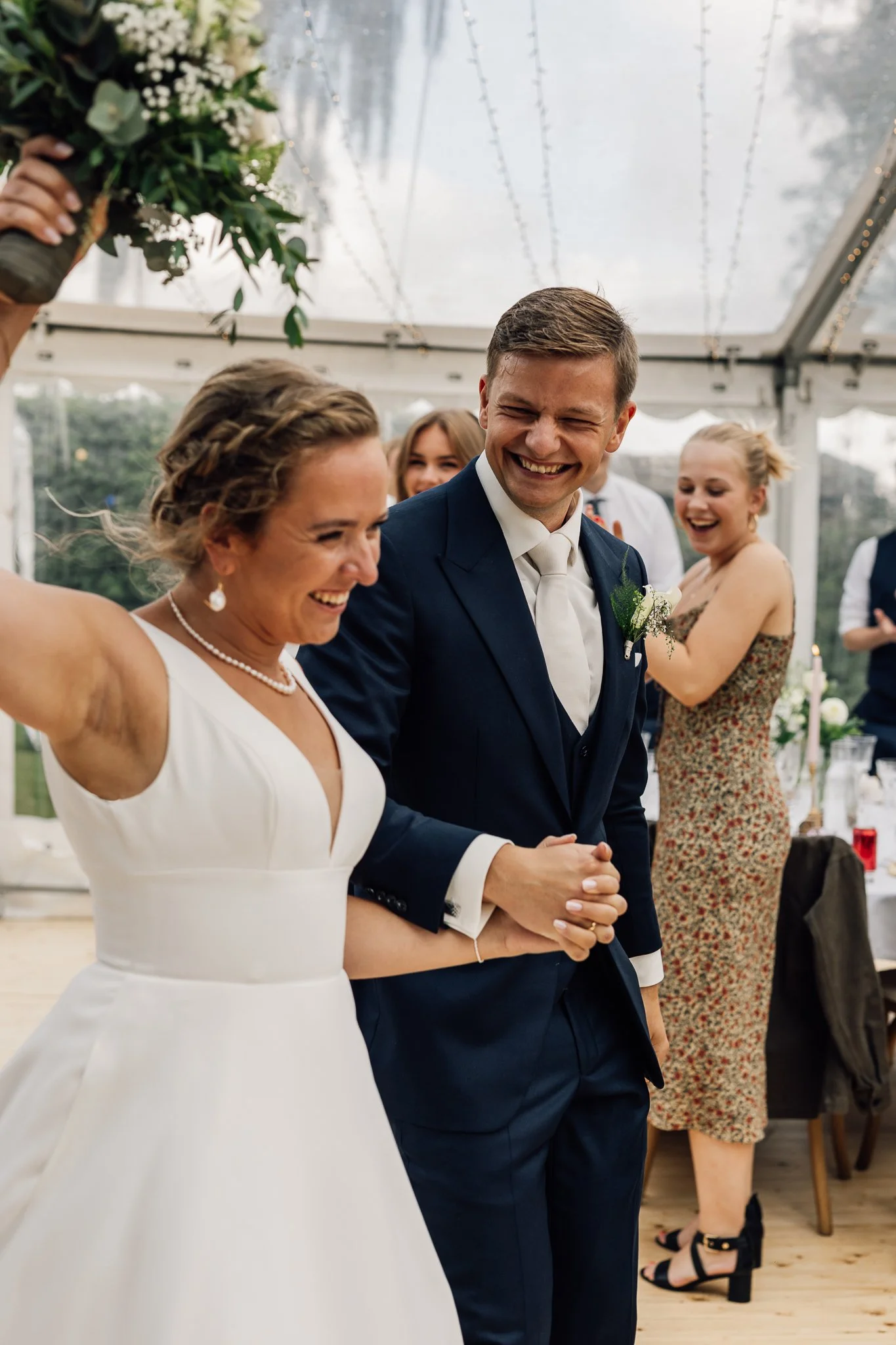 Et brudepar danser under en telt med lysslynge, omgivet af glade gæster.