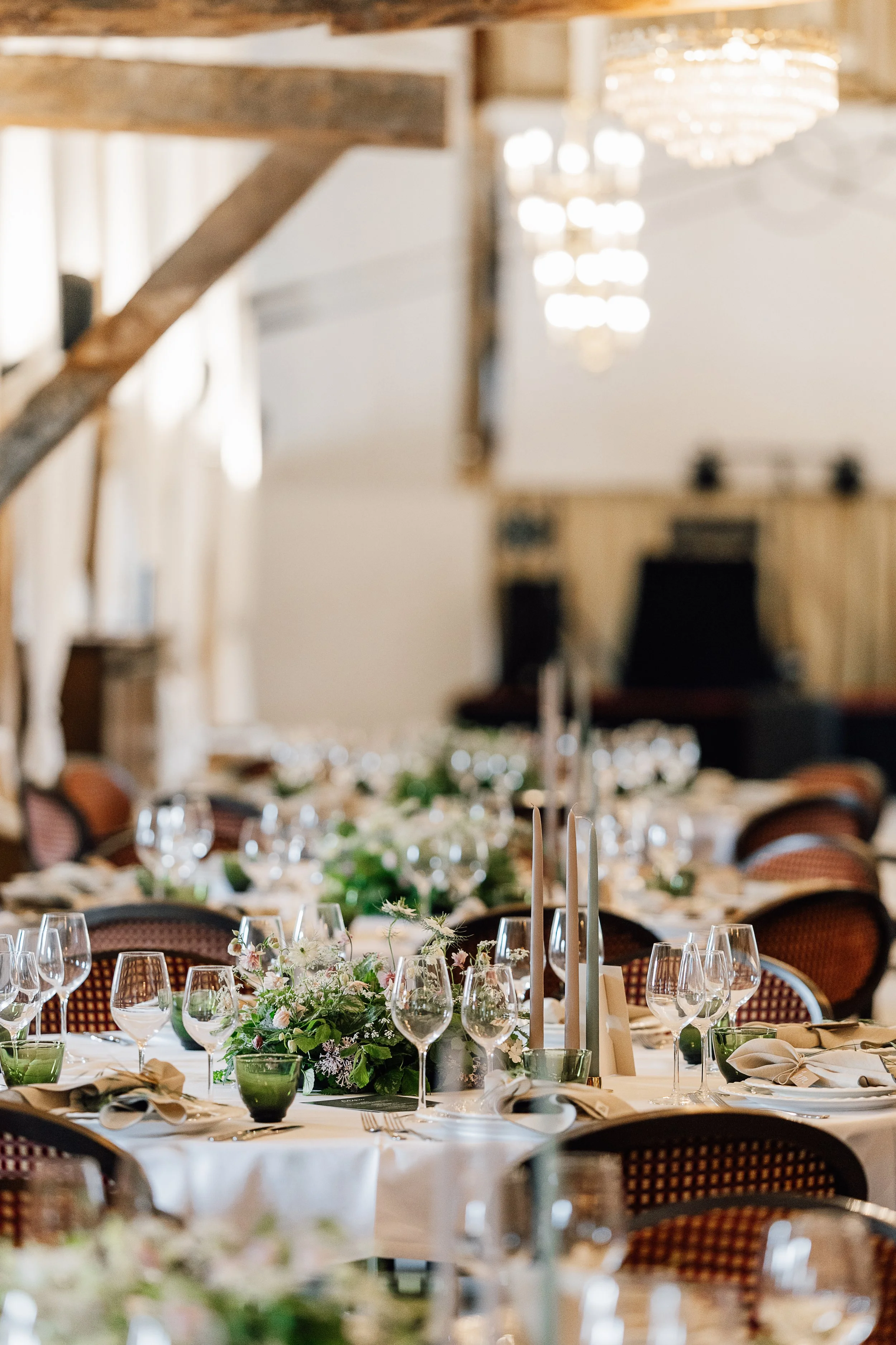 Borddækning til fest med hvideduge, blomsterdekorationer, stearinlys, glas og bestik i en elegant banquetlignende setting.